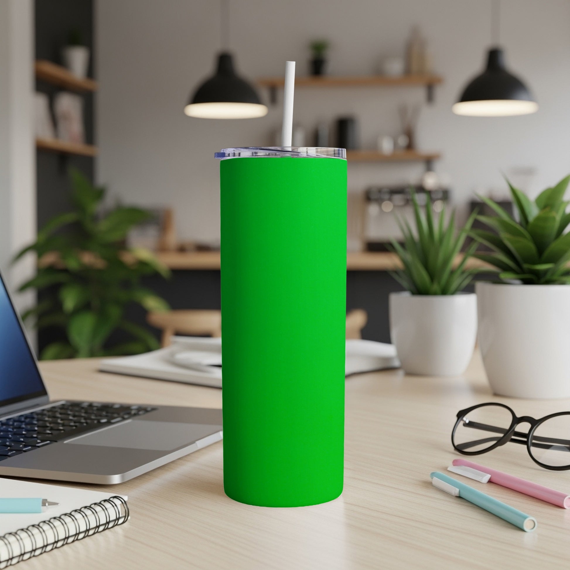 Green tumbler with straw on a desk next to a laptop.
