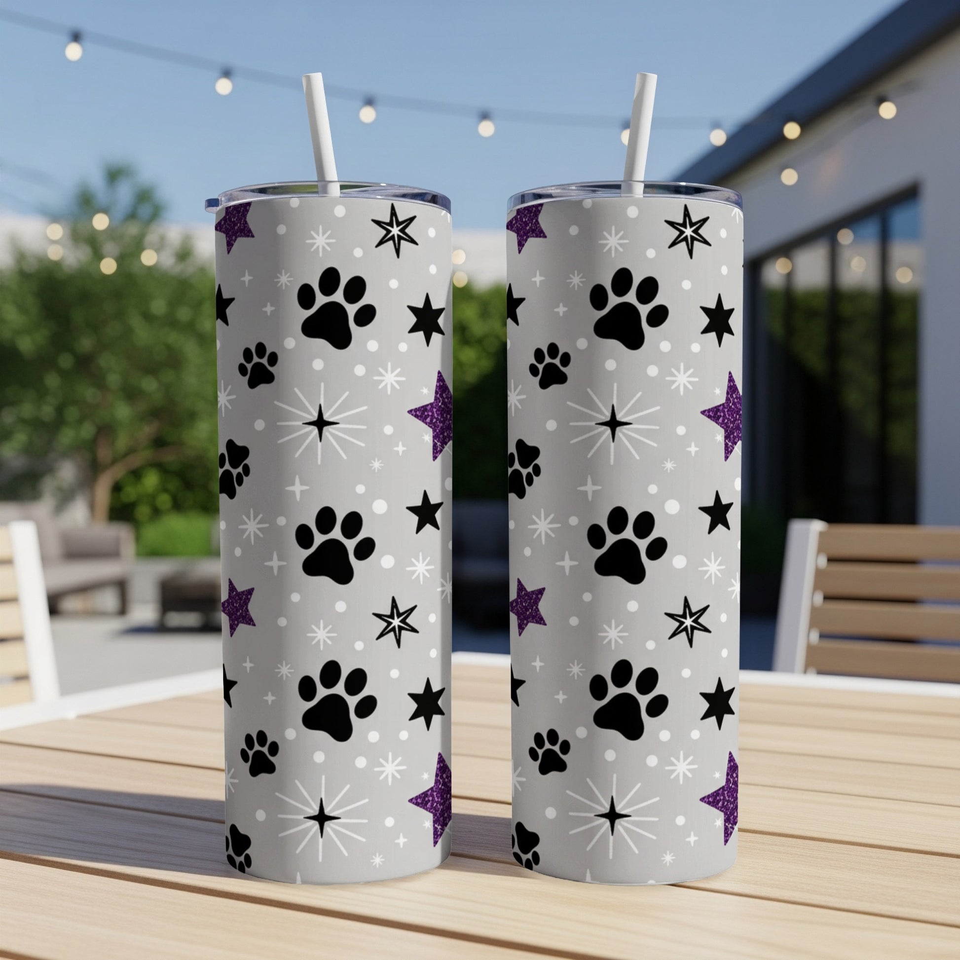 Two tall, silver tumblers with paw prints, stars, and purple glitter.