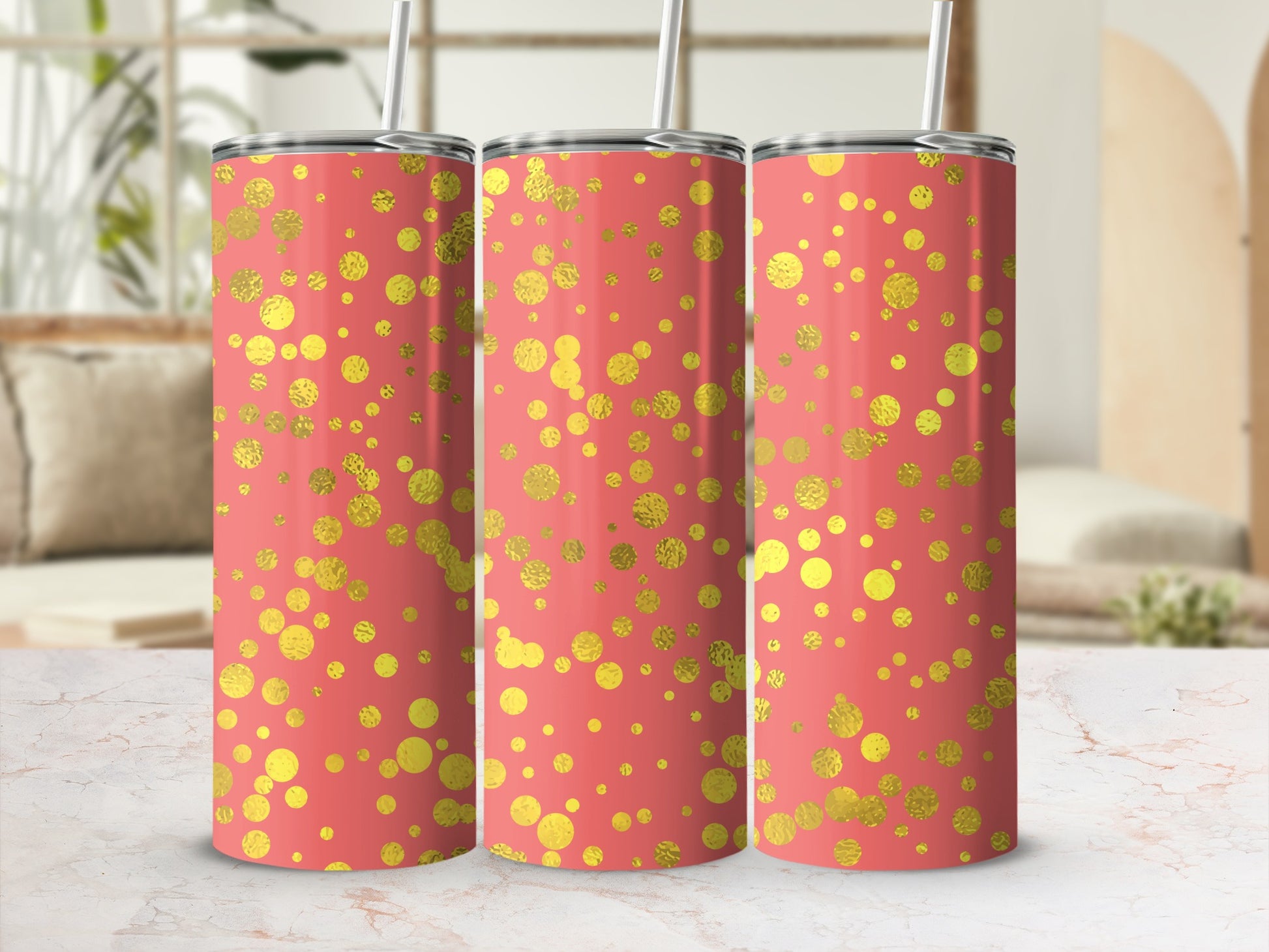 Three coral tumblers with gold glitter polka dots and straws, on a marble surface with a blurred background.
