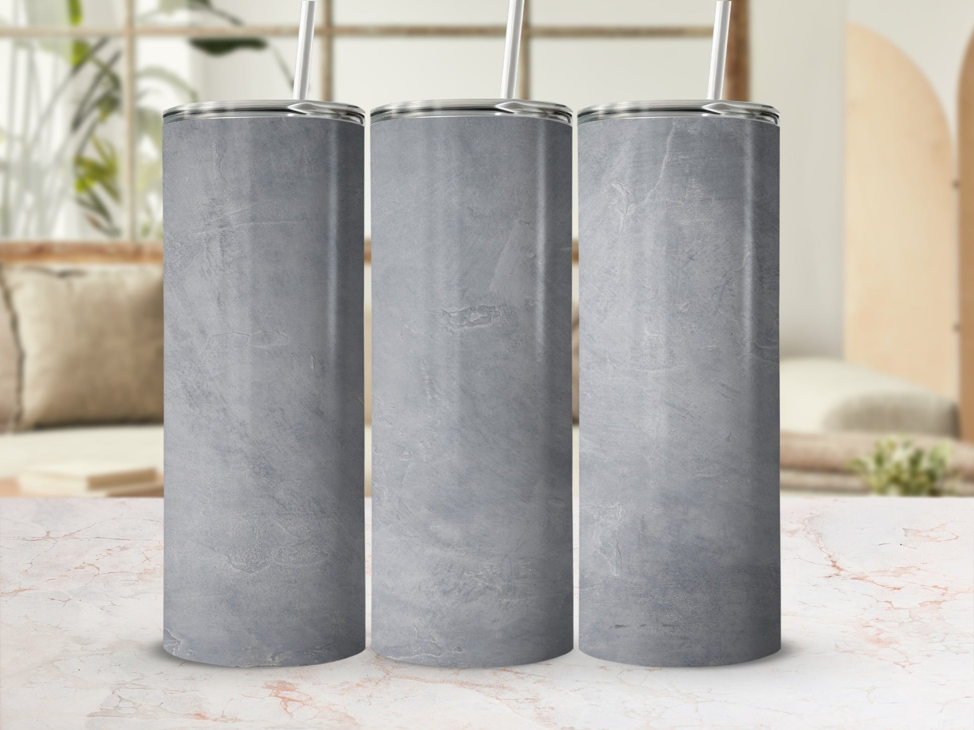 Three gray concrete textured tumblers with straws on a marbled countertop.