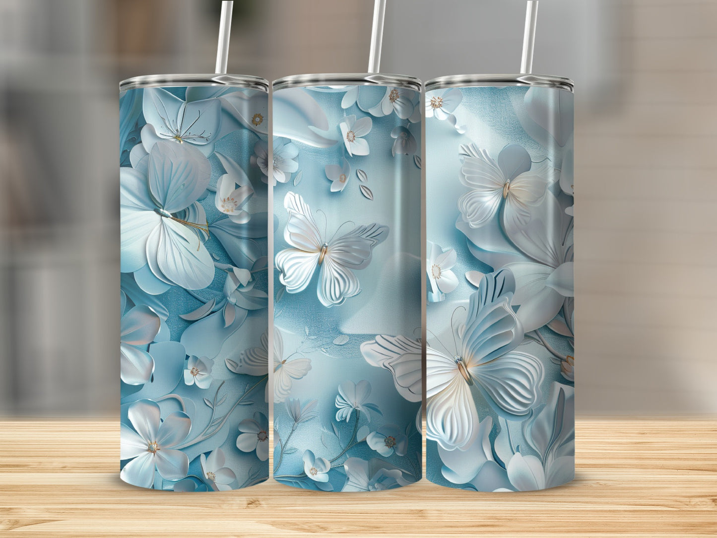 Three tall tumblers with blue floral and butterfly designs on a wooden surface.