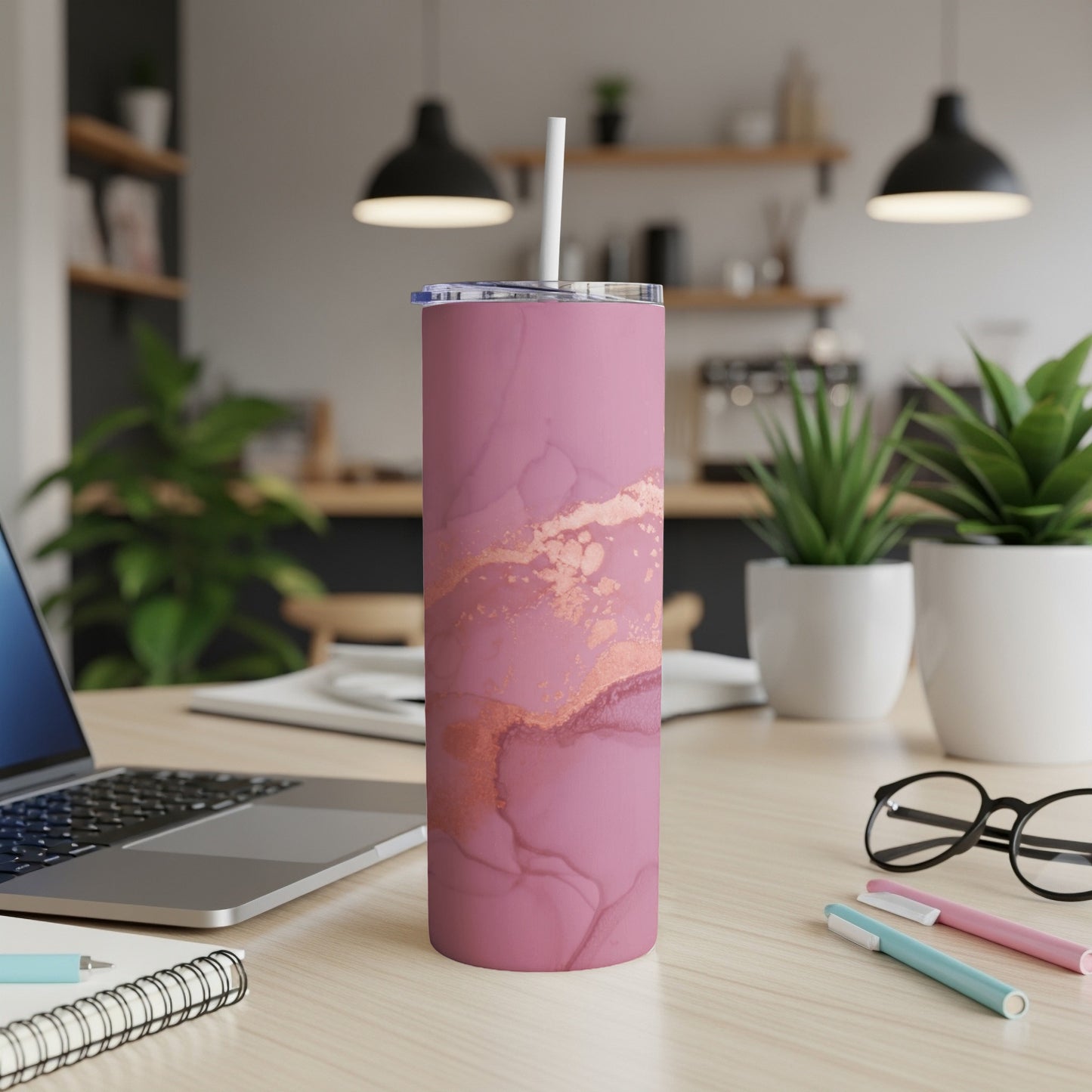 Pink and rose gold marble tumbler with straw on a desk.