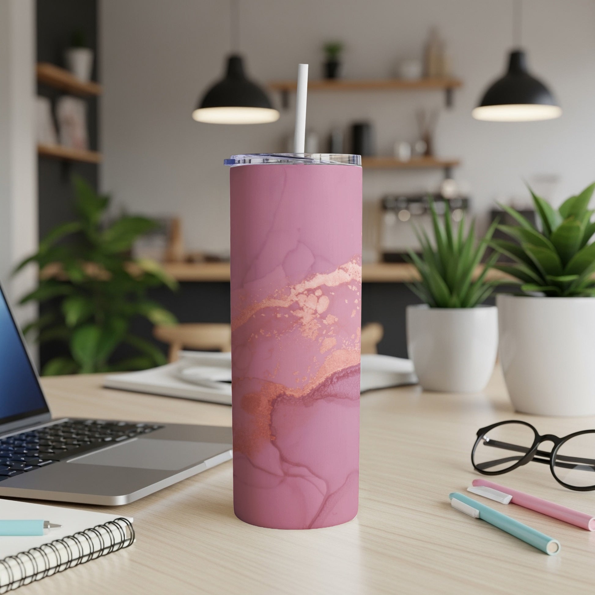 Pink and rose gold marble tumbler with straw on a desk.