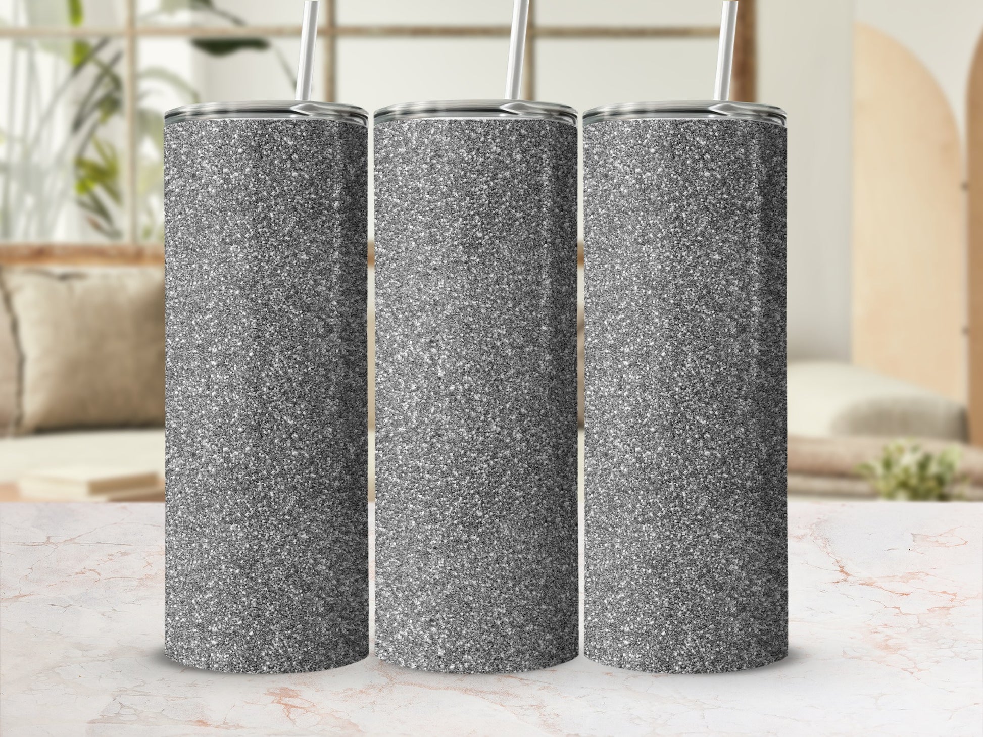 Three glittery silver tumblers with straws stand in a row.