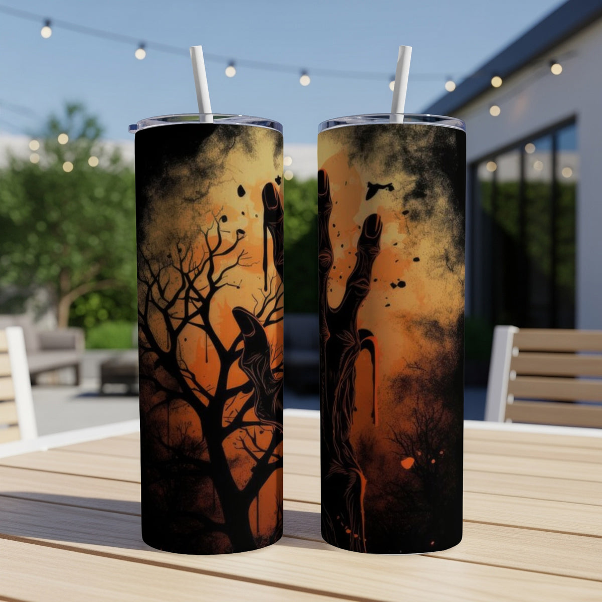 Two tumblers with a spooky zombie hand and bare tree design on an outdoor table.