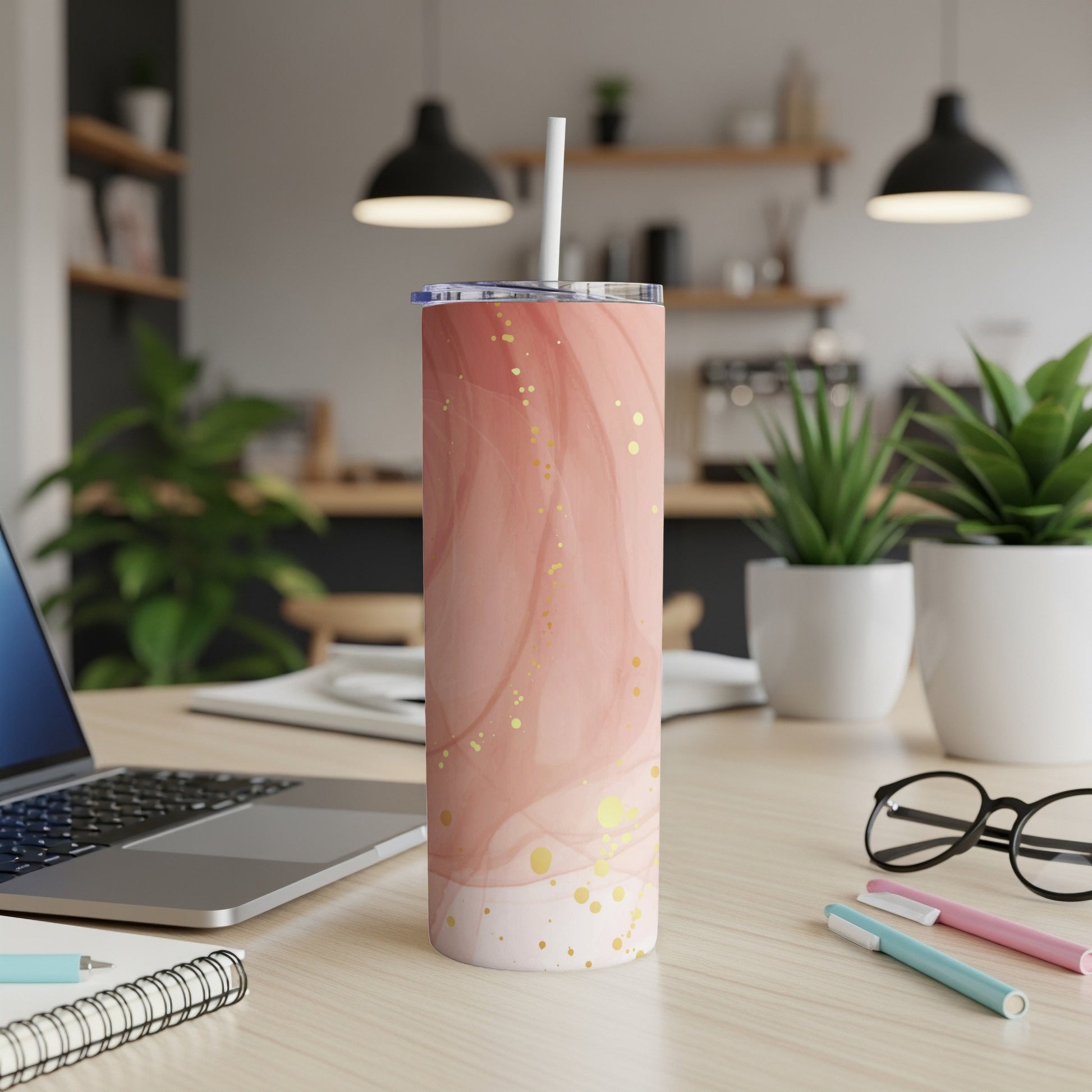 Pink and gold marbled tumbler with straw on desk with laptop and pens.