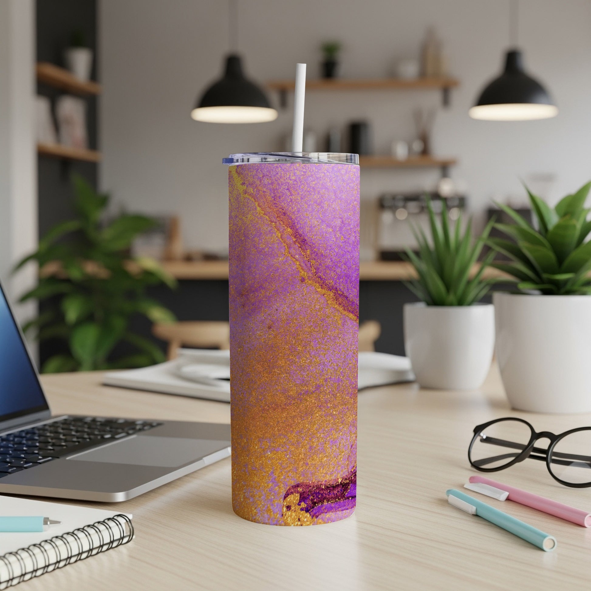 Purple and gold abstract patterned tumbler with straw on a desk.