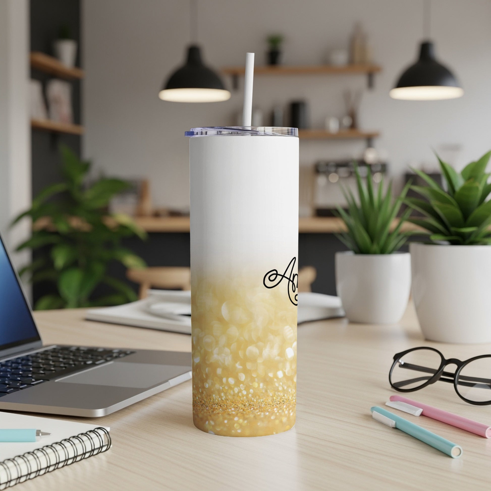 White tumbler with gold glitter and "A" calligraphy design on a desk.