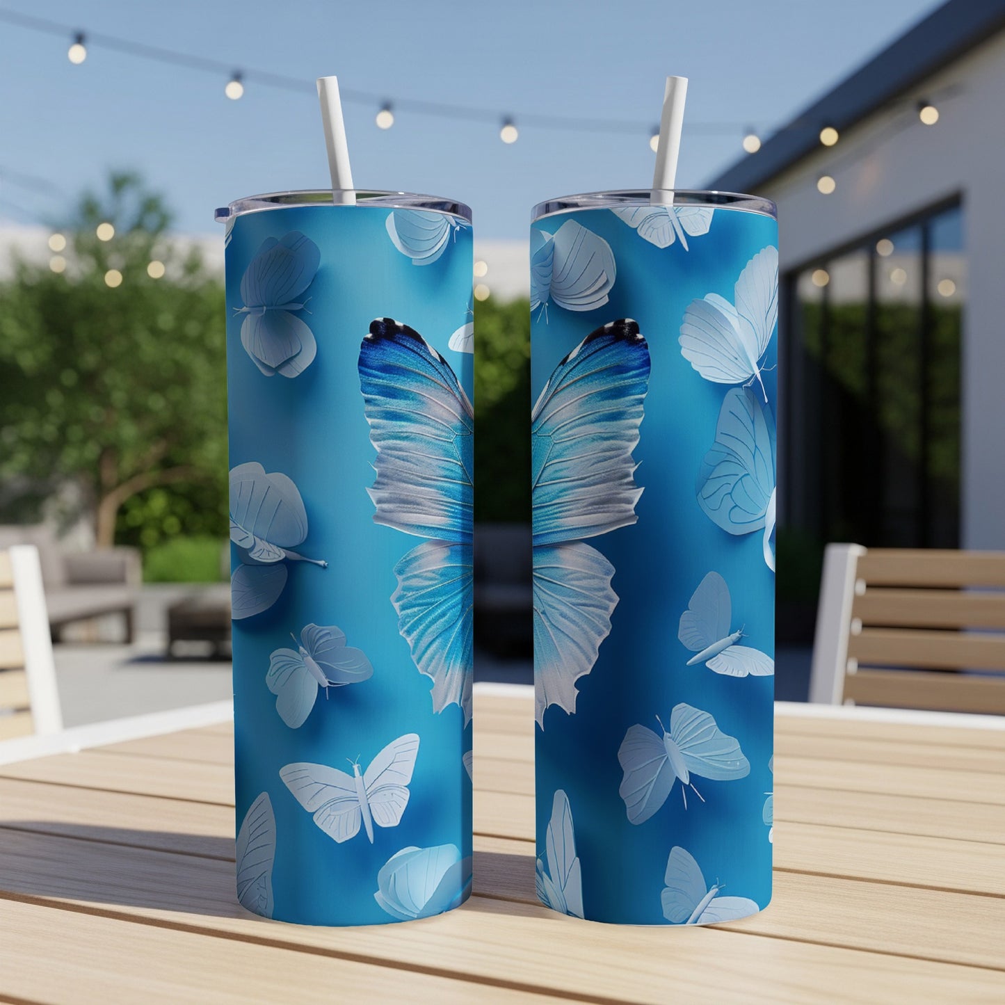 Two blue tumblers with butterfly designs on a table outdoors.