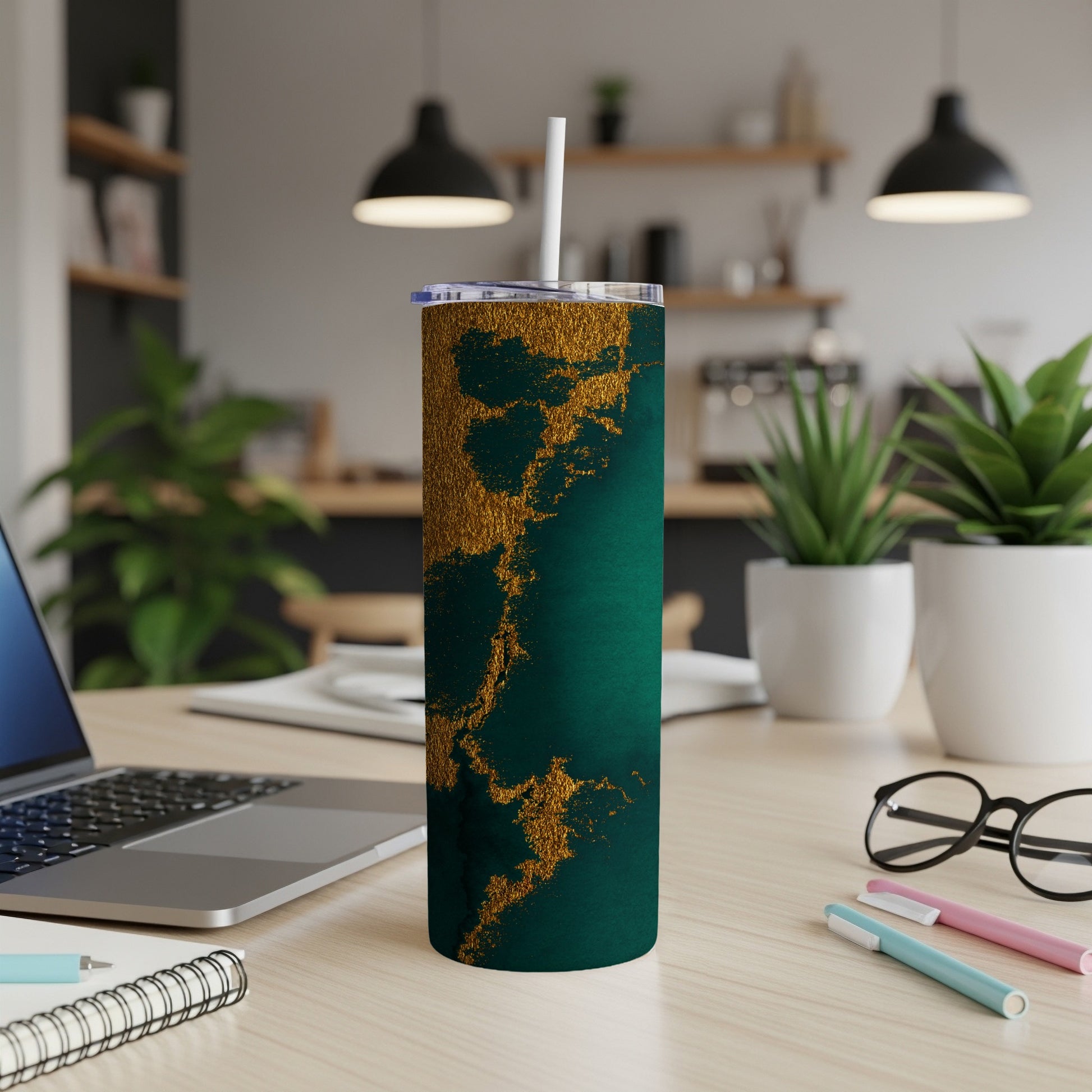 Green and gold marbled tumbler with straw on a desk.