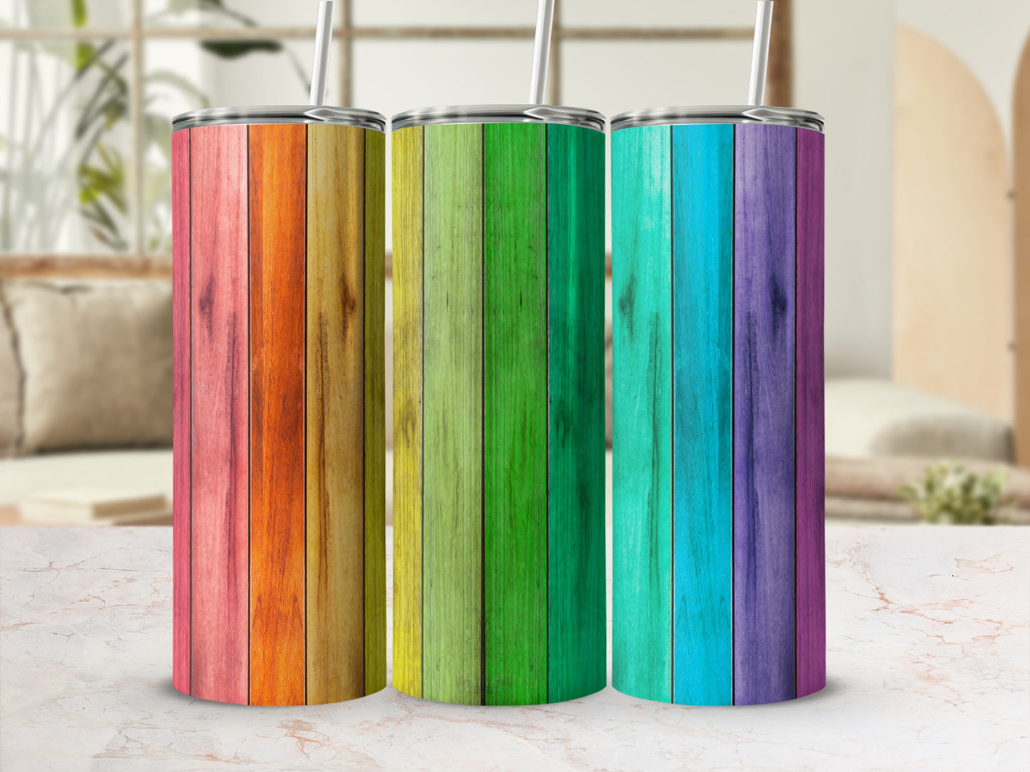 Three rainbow-striped wooden tumblers with straws stand on a marble surface.