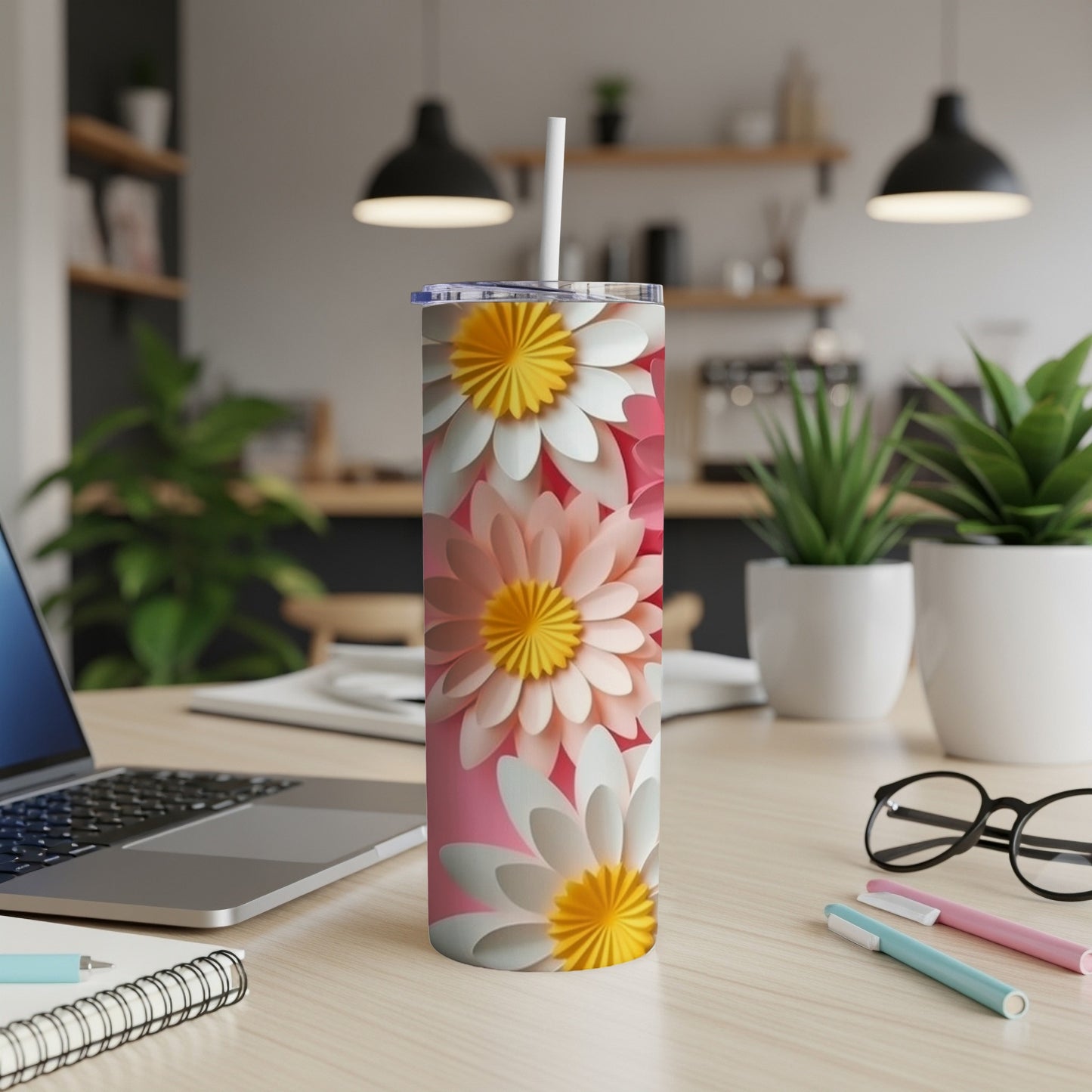 Pink tumbler with white, pink, and yellow layered flowers, on a desk.