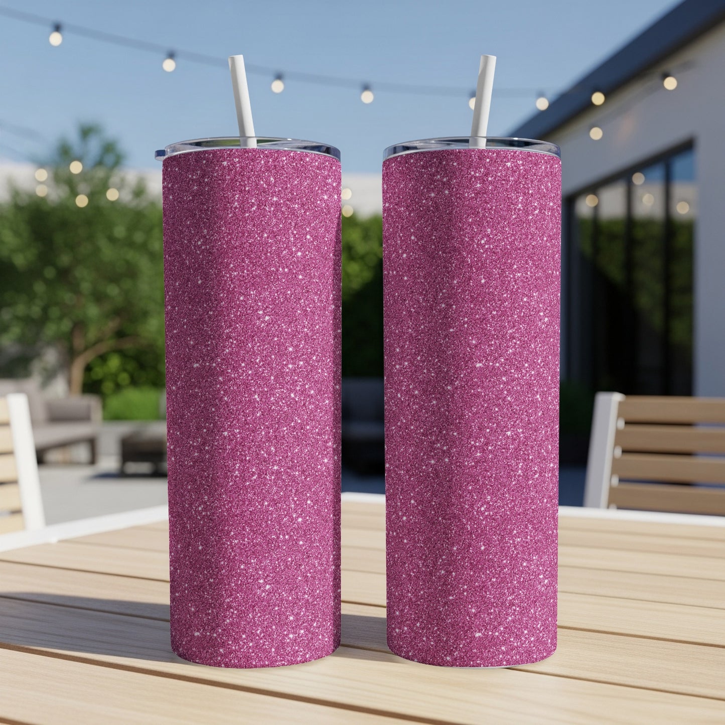 Two glittery pink tumblers with white straws sit on a wooden table outside.