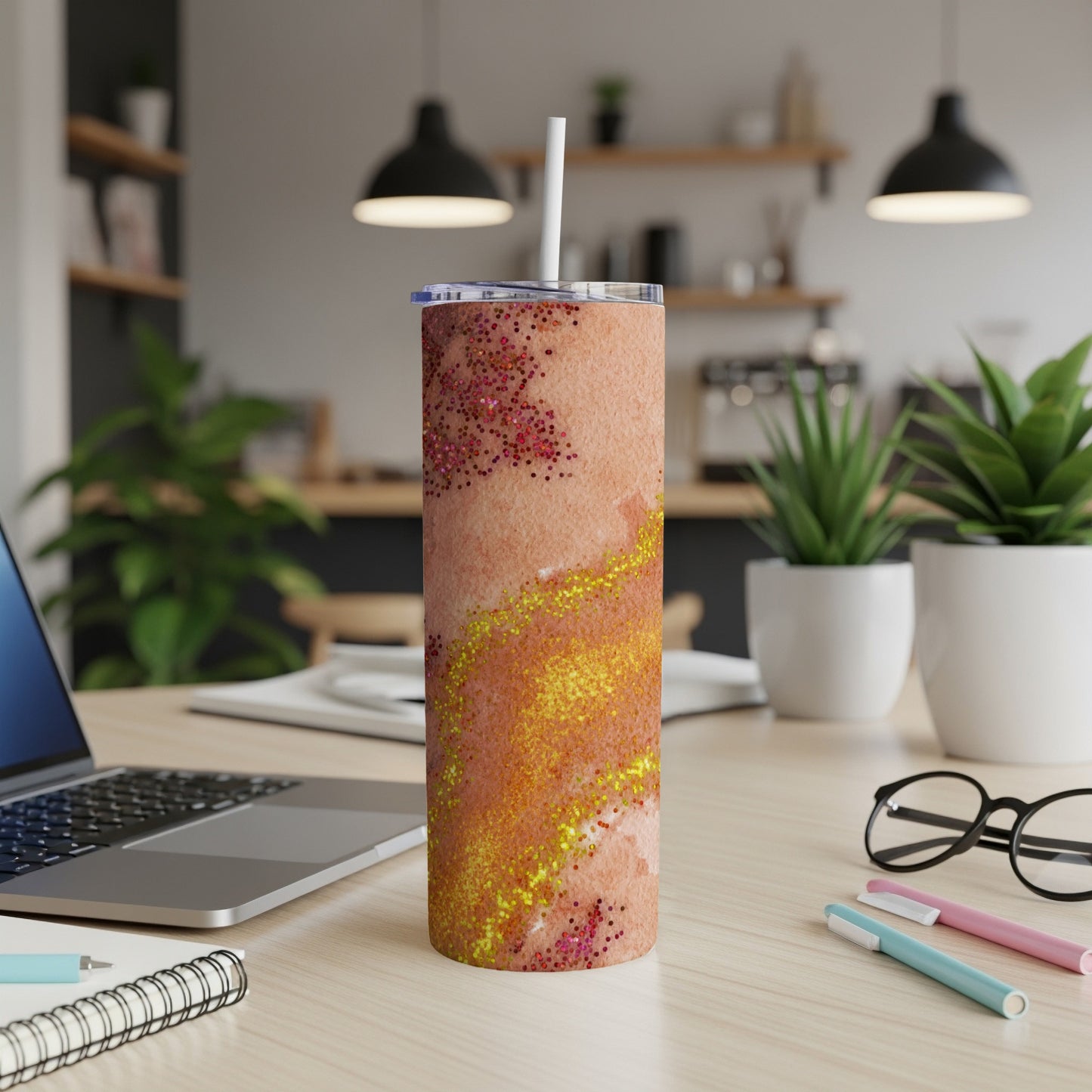 Glittery orange and pink marbled tumbler with straw on desk.