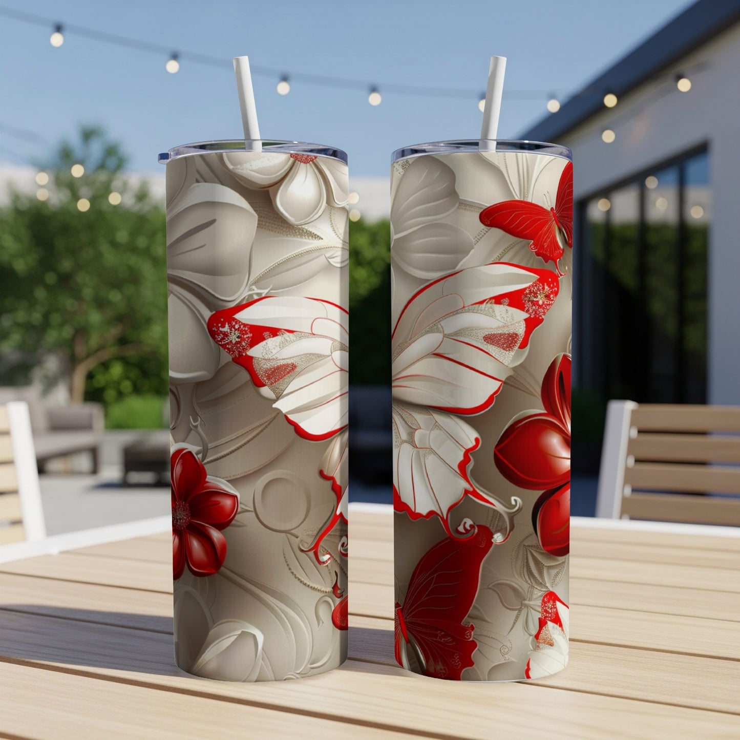 Two tumblers with red and white floral and butterfly designs on a patio table.