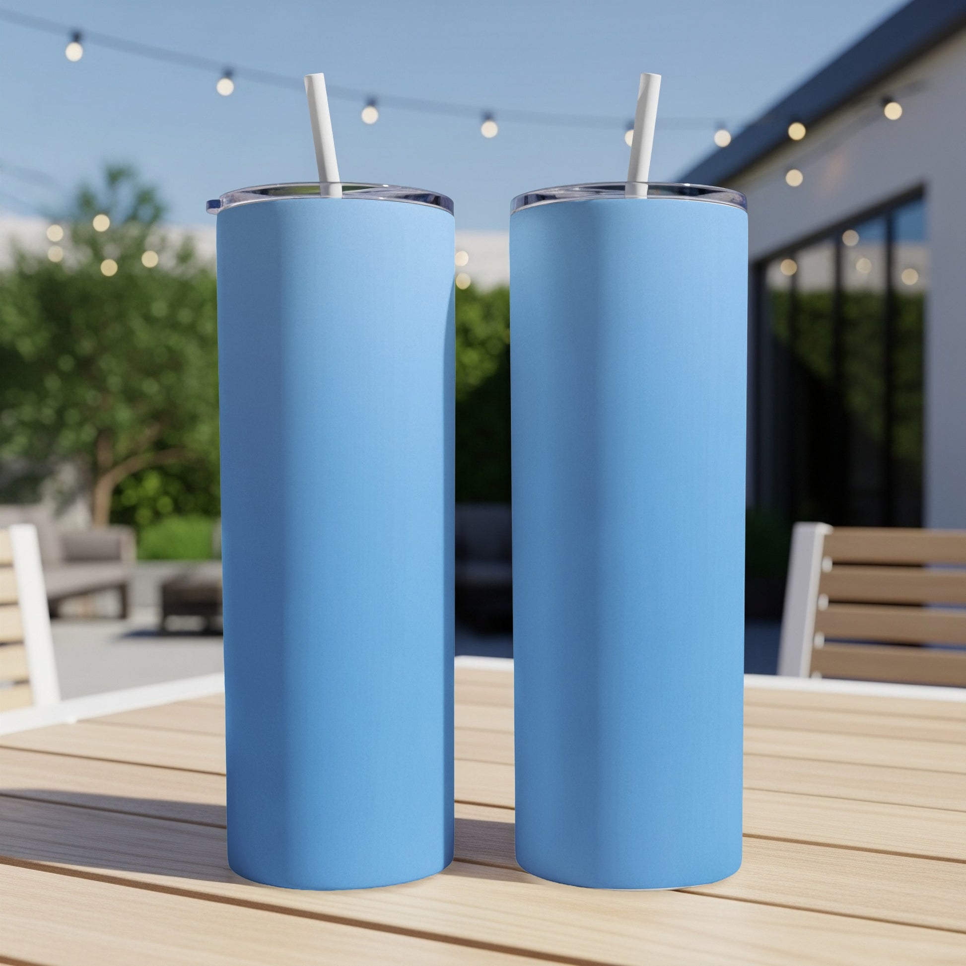 Two blue stainless steel tumblers with white straws on a wooden table.