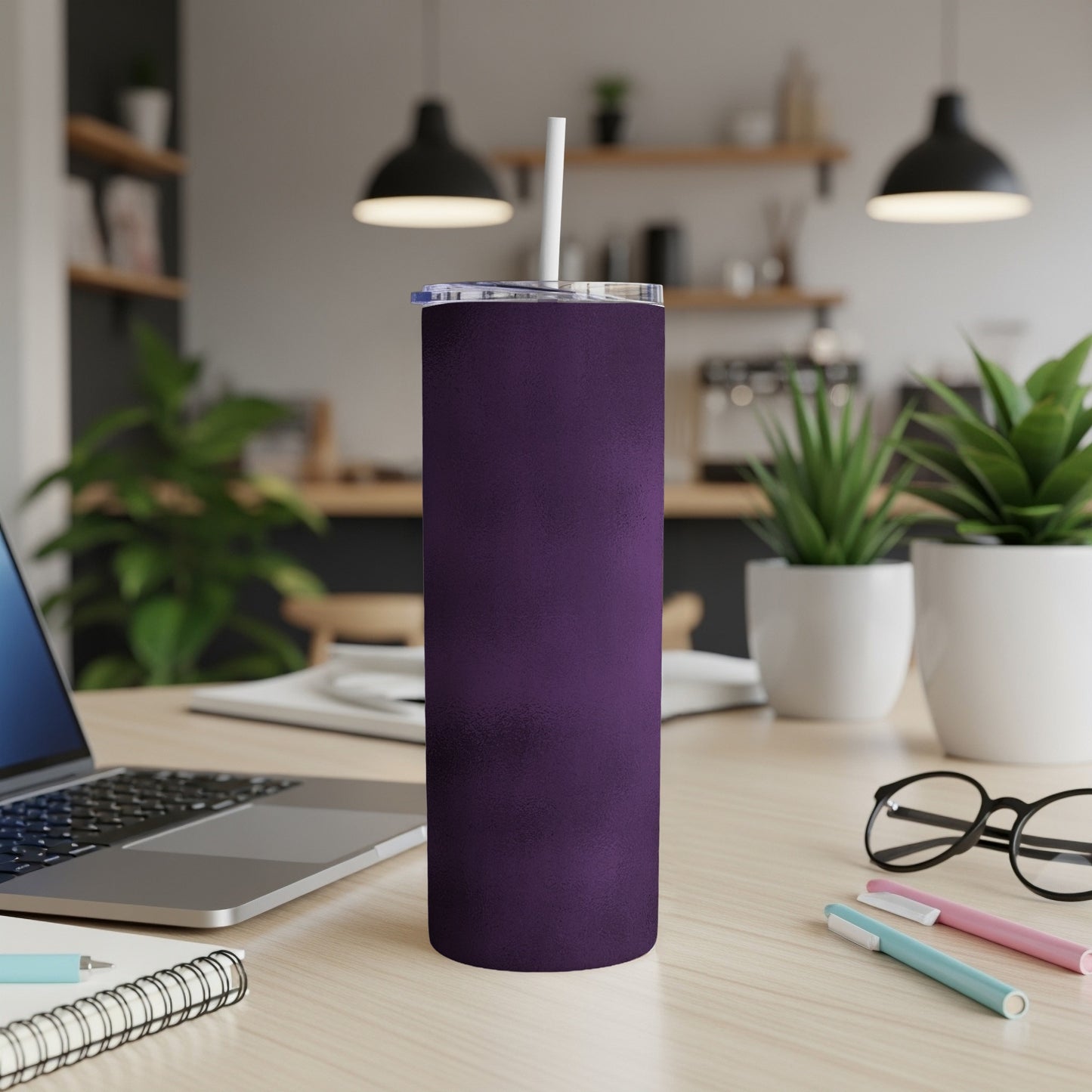 Purple skinny tumbler with straw on a desk next to a laptop.
