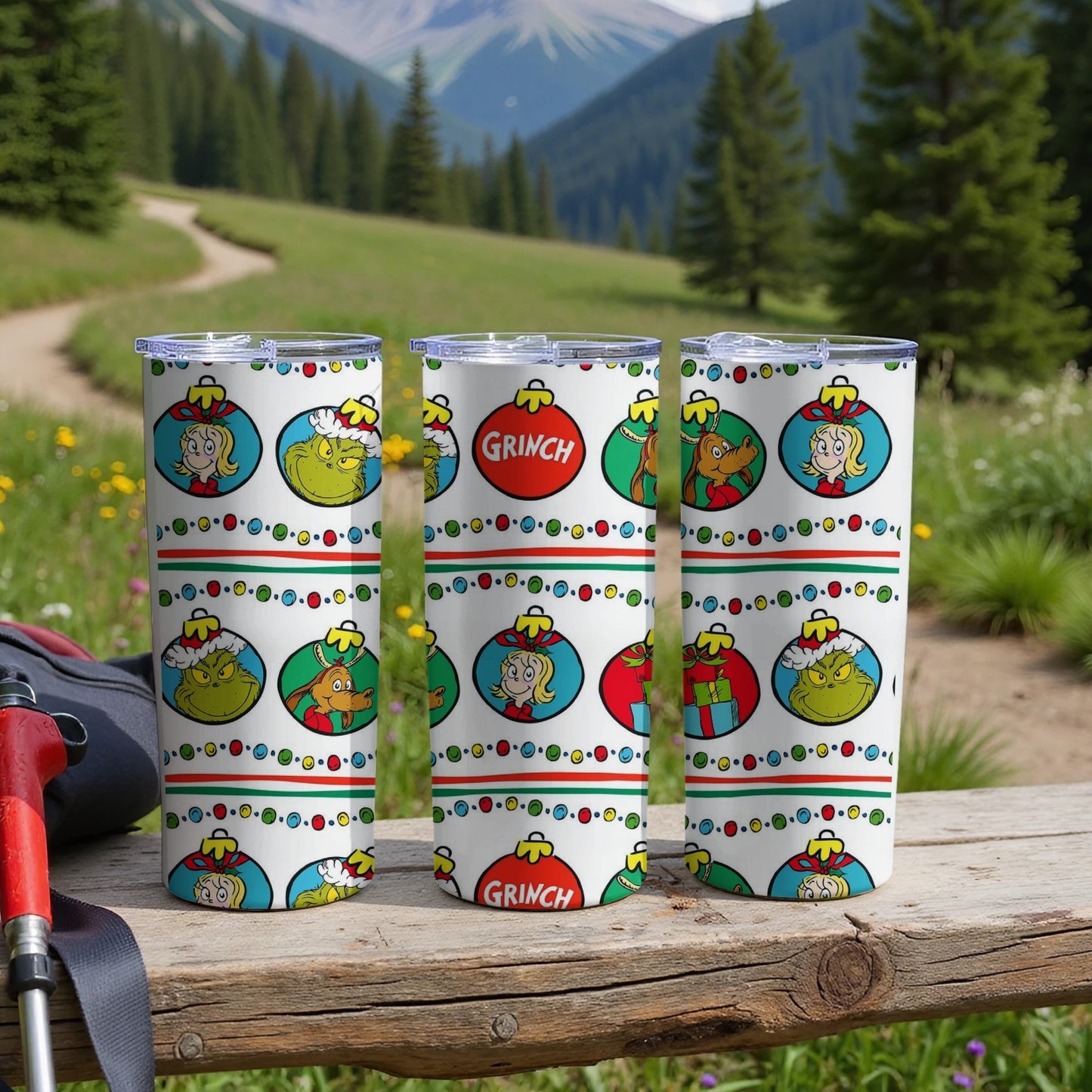 Three Grinch-themed tumblers with Christmas ornaments on a wooden surface.