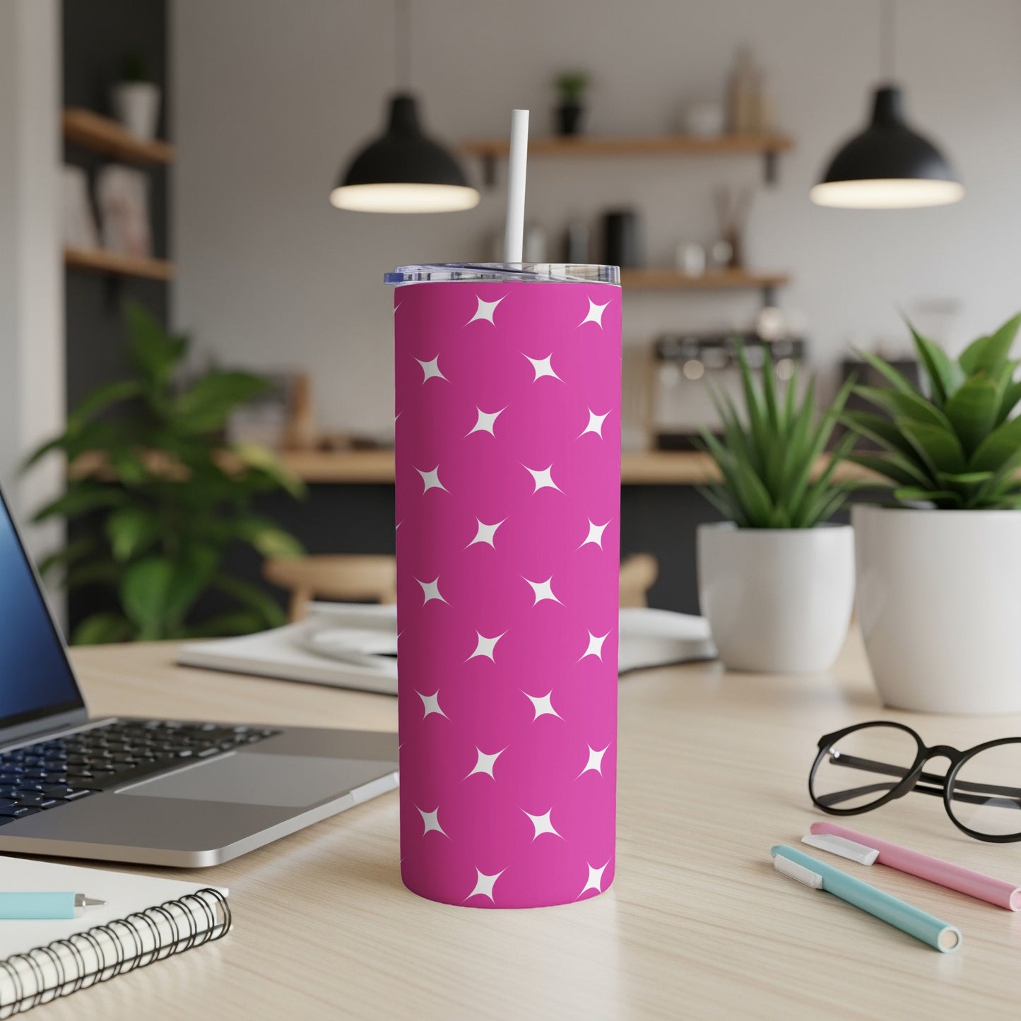 Pink tumbler with white stars, laptop, and pens on desk.