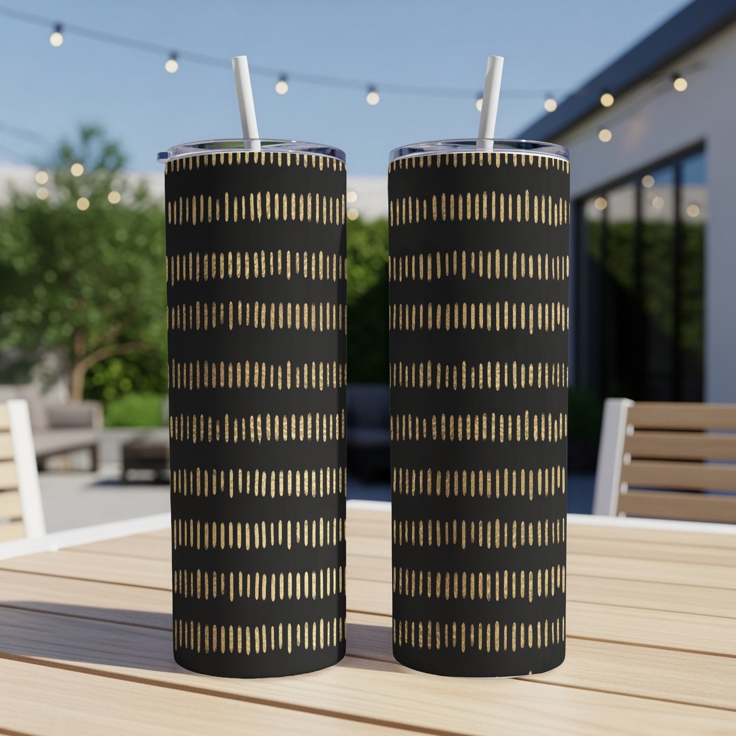 Two black tumblers with gold dash pattern and white straws on a wooden table.