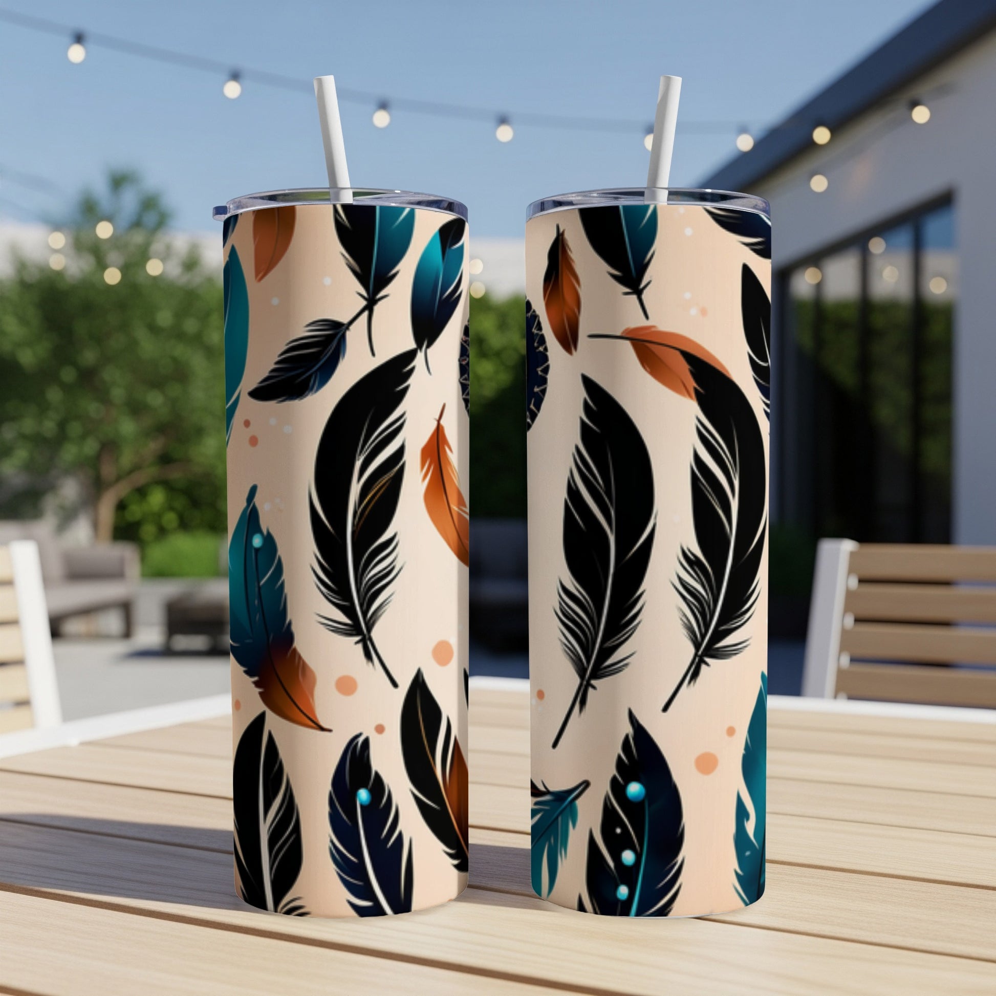 Two tan tumblers with feather pattern and straws, outdoors on table.