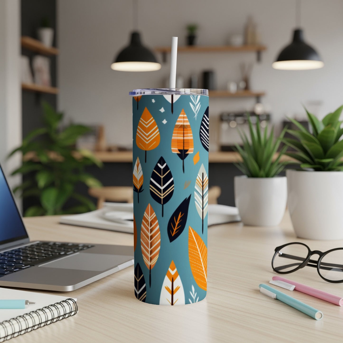 Blue tumbler with orange, white, and black leaf pattern, white straw, on desk.