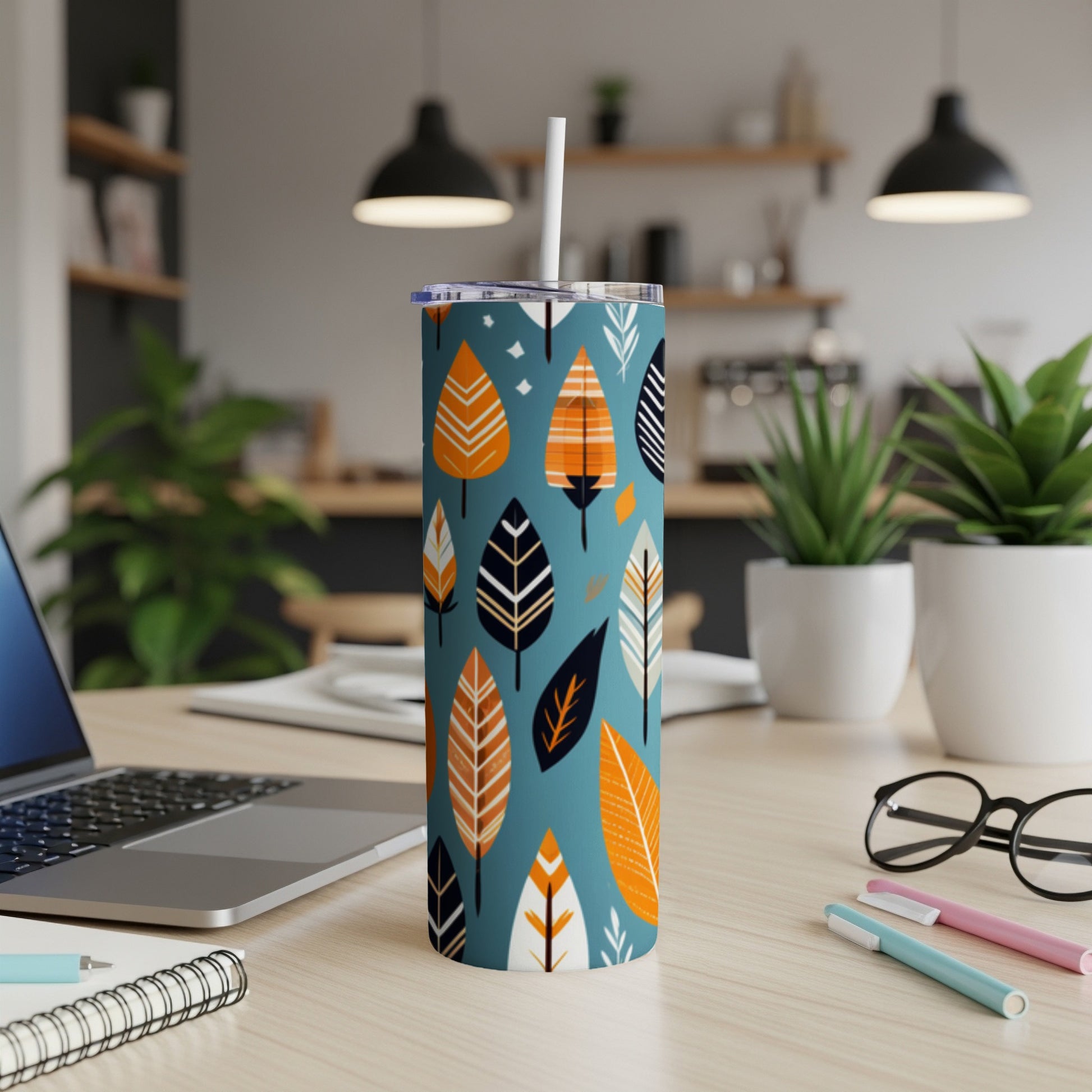 Blue tumbler with orange, white, and black leaf pattern, white straw, on desk.