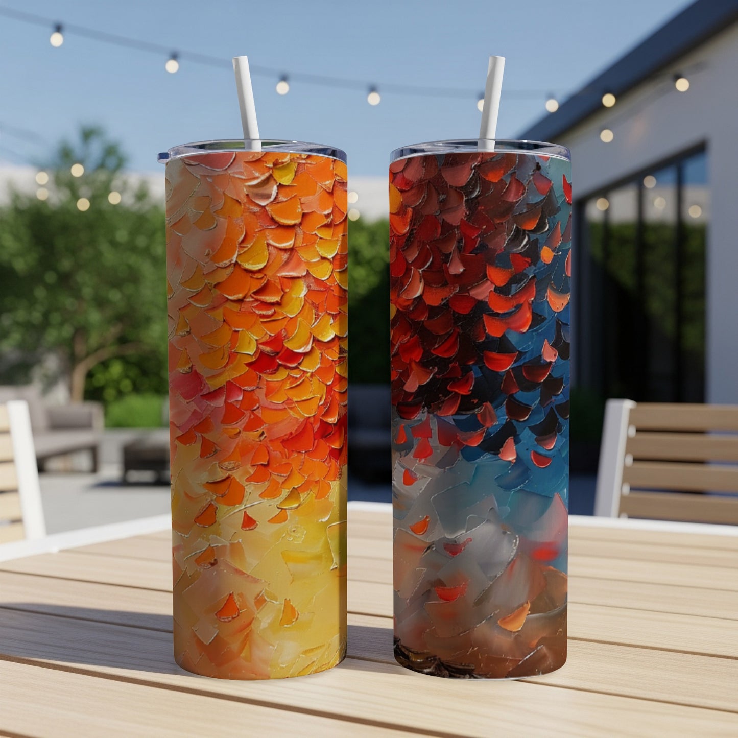 Two tall tumblers with fiery abstract art designs sit on a table outdoors.