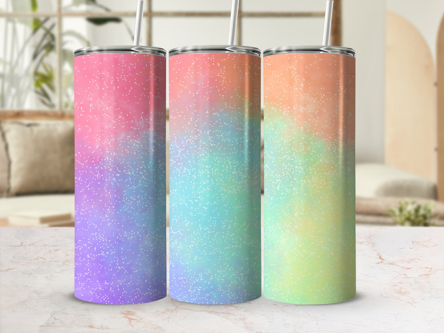 Three tumblers with pastel ombre glitter designs and silver straws, on a marble surface.