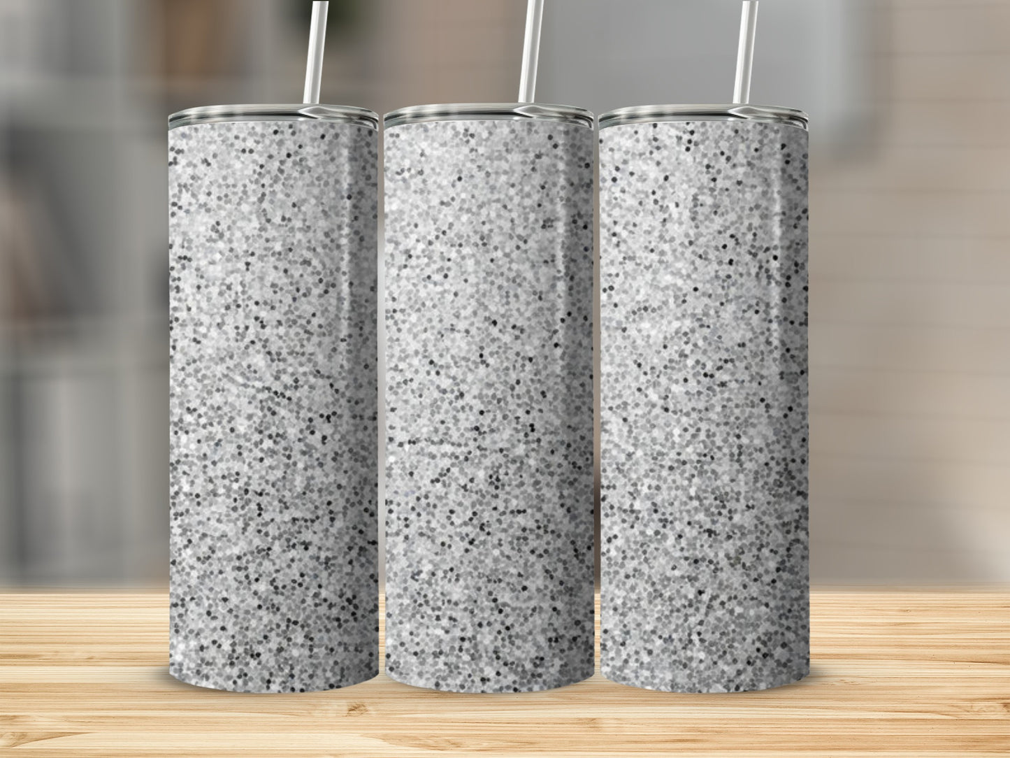 Three silver glitter tumblers with straws on a wooden surface.