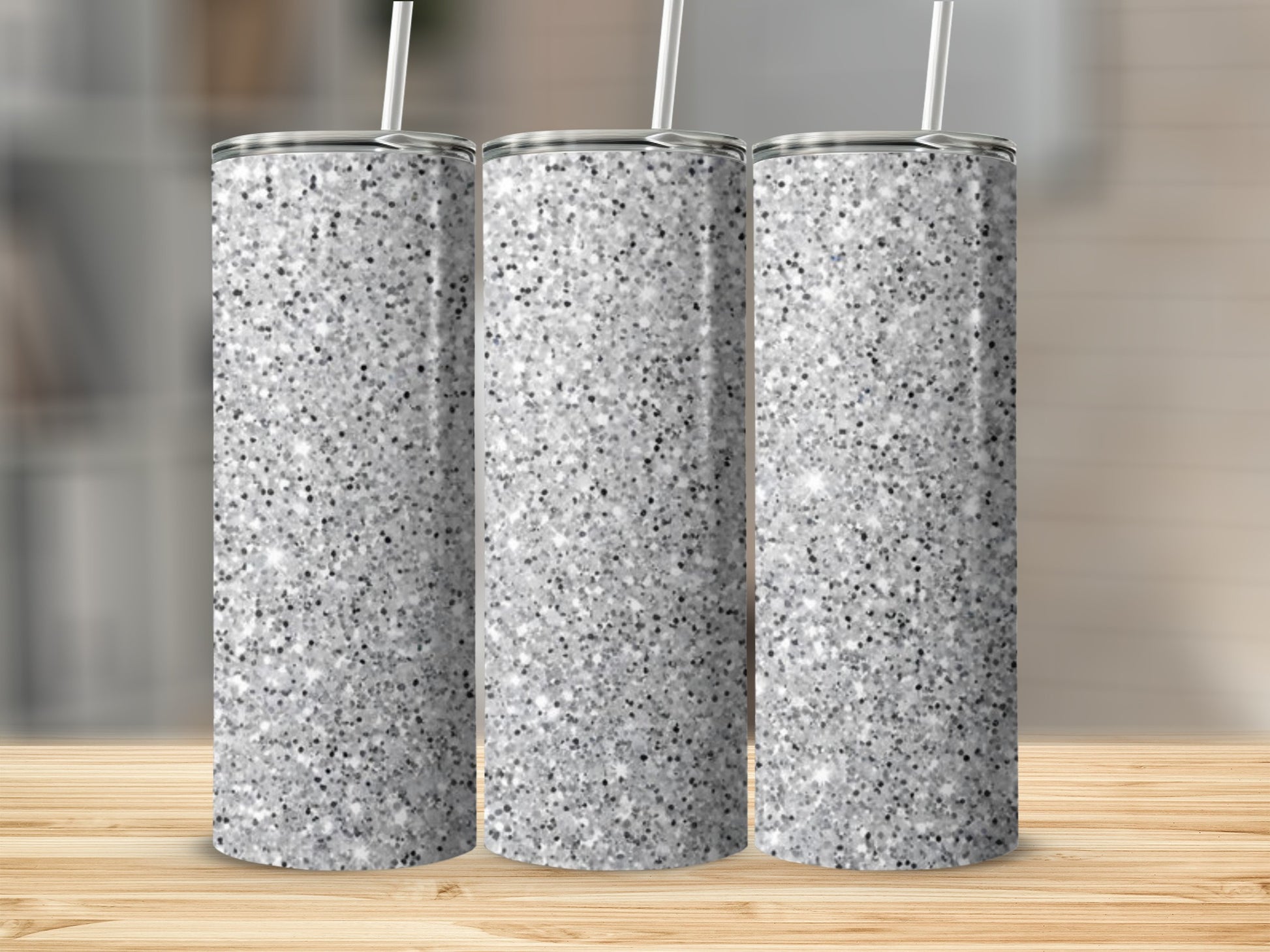 Three silver glitter tumblers with straws on a wooden surface.