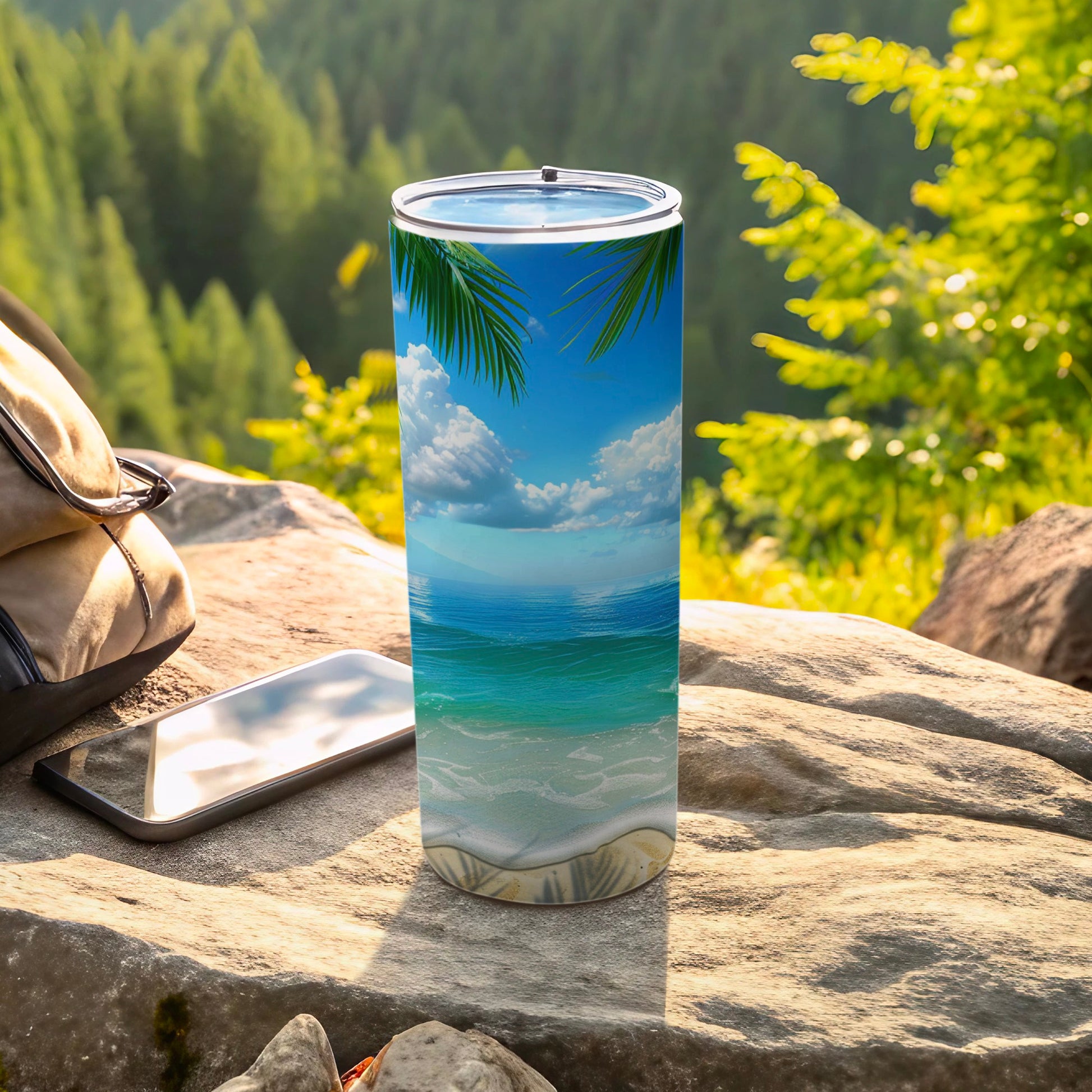 Tall tumbler with ocean beach palm tree scene on rocks with phone and backpack.
