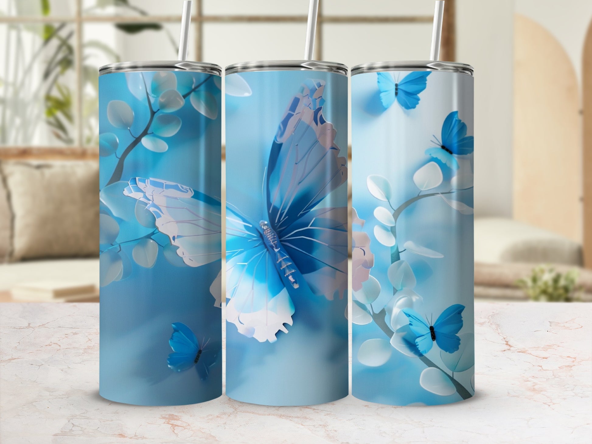 Three blue tumblers with butterfly and floral designs on a marble surface.