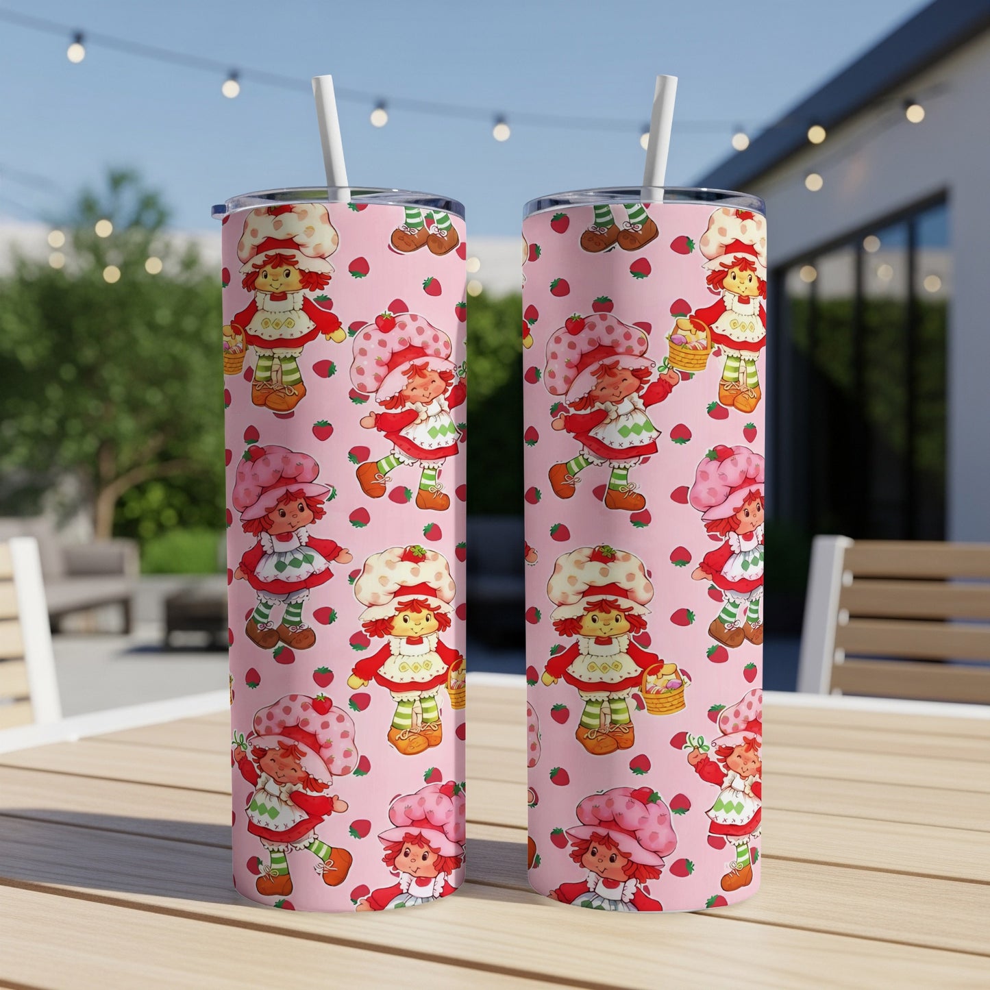 Two pink tumblers with Strawberry Shortcake pattern on a table outdoors.