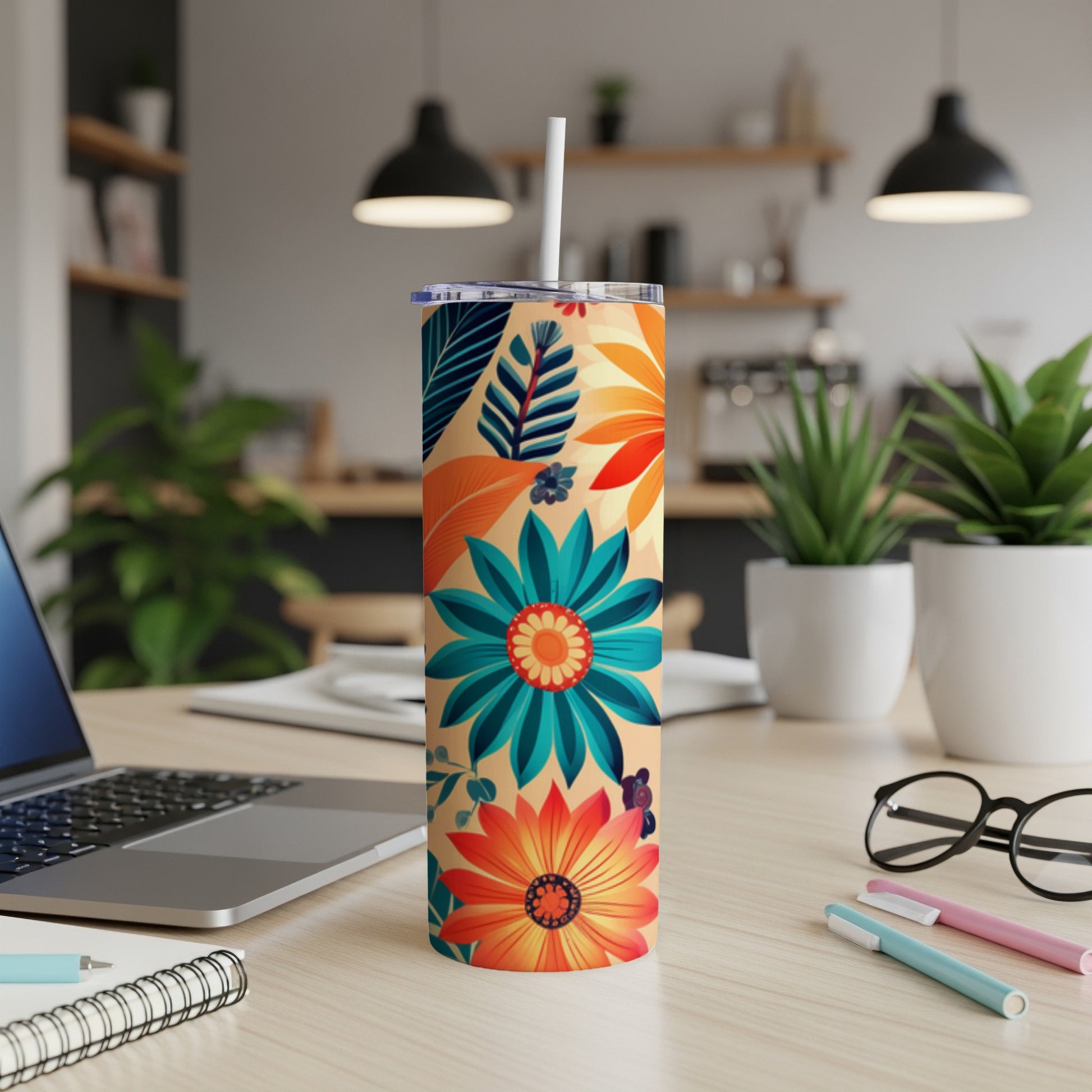Tall tumbler with colorful floral pattern, straw, and laptop on desk.