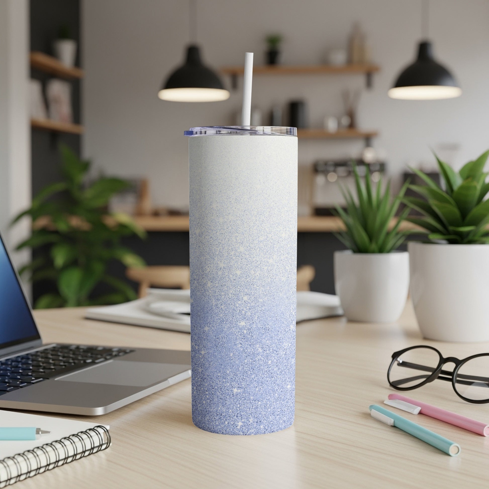 Gradient blue glitter tumbler with straw on desk with laptop and pens.