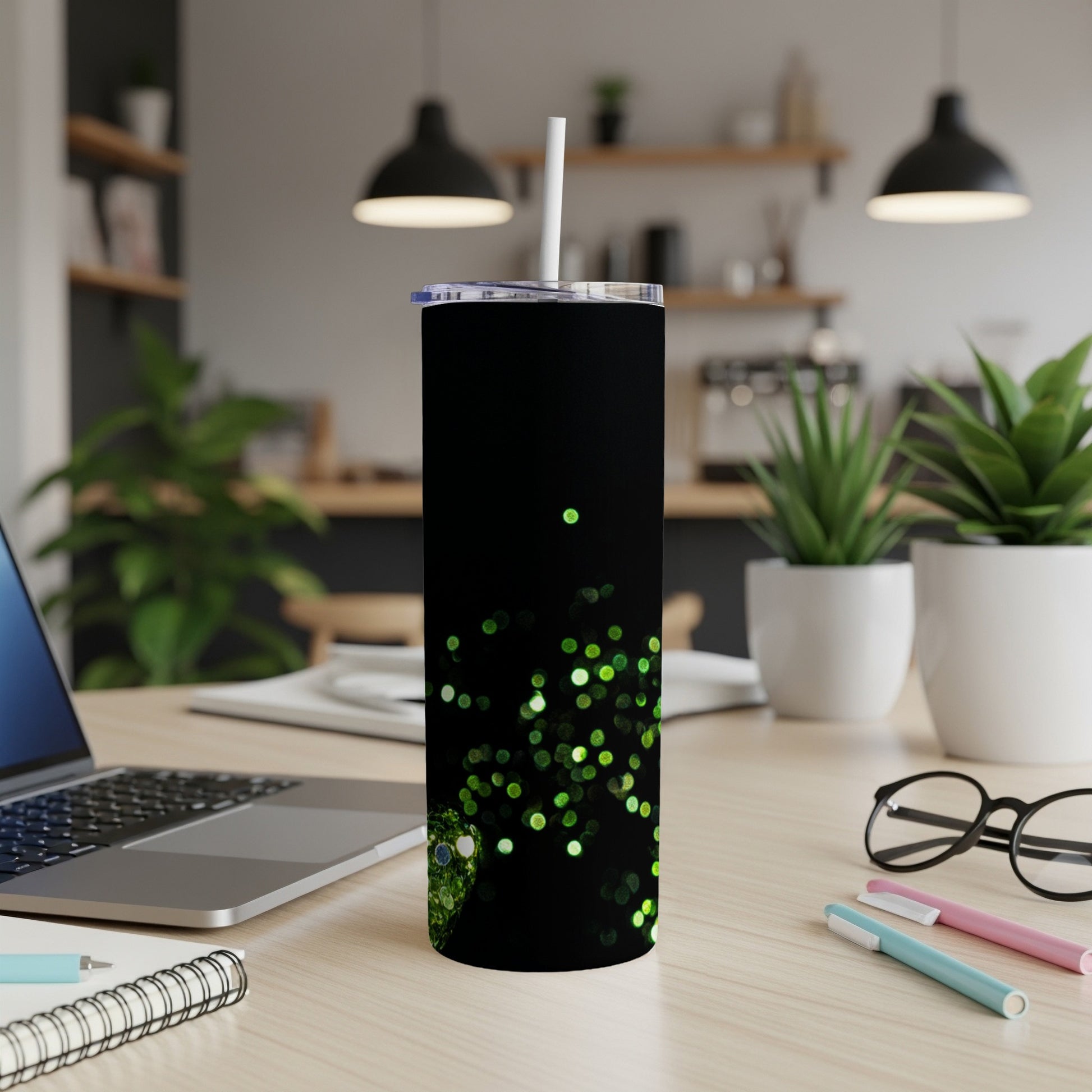 Black tumbler with green glitter design, straw, on a desk.