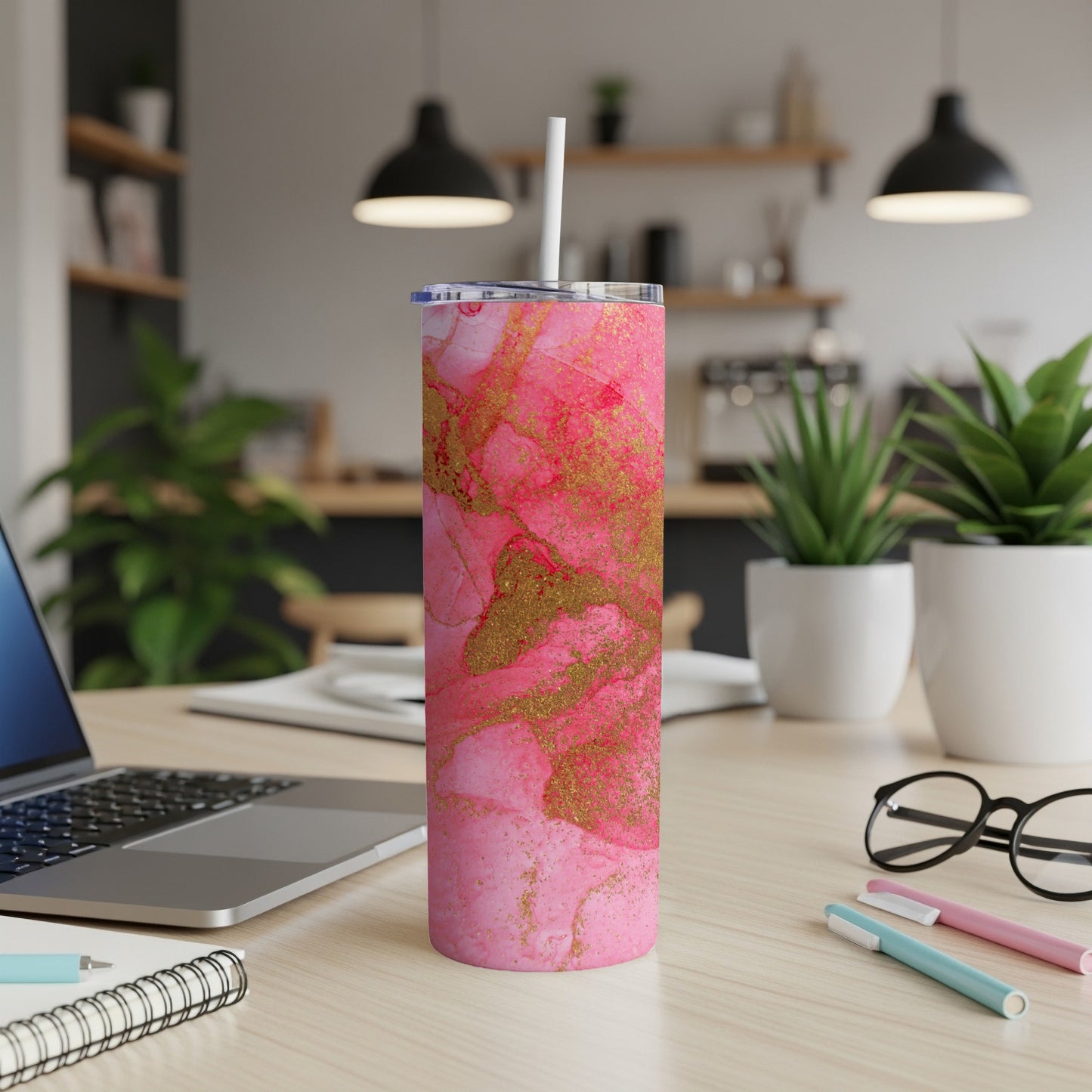 Pink and gold marble pattern insulated tumbler with straw on desk.