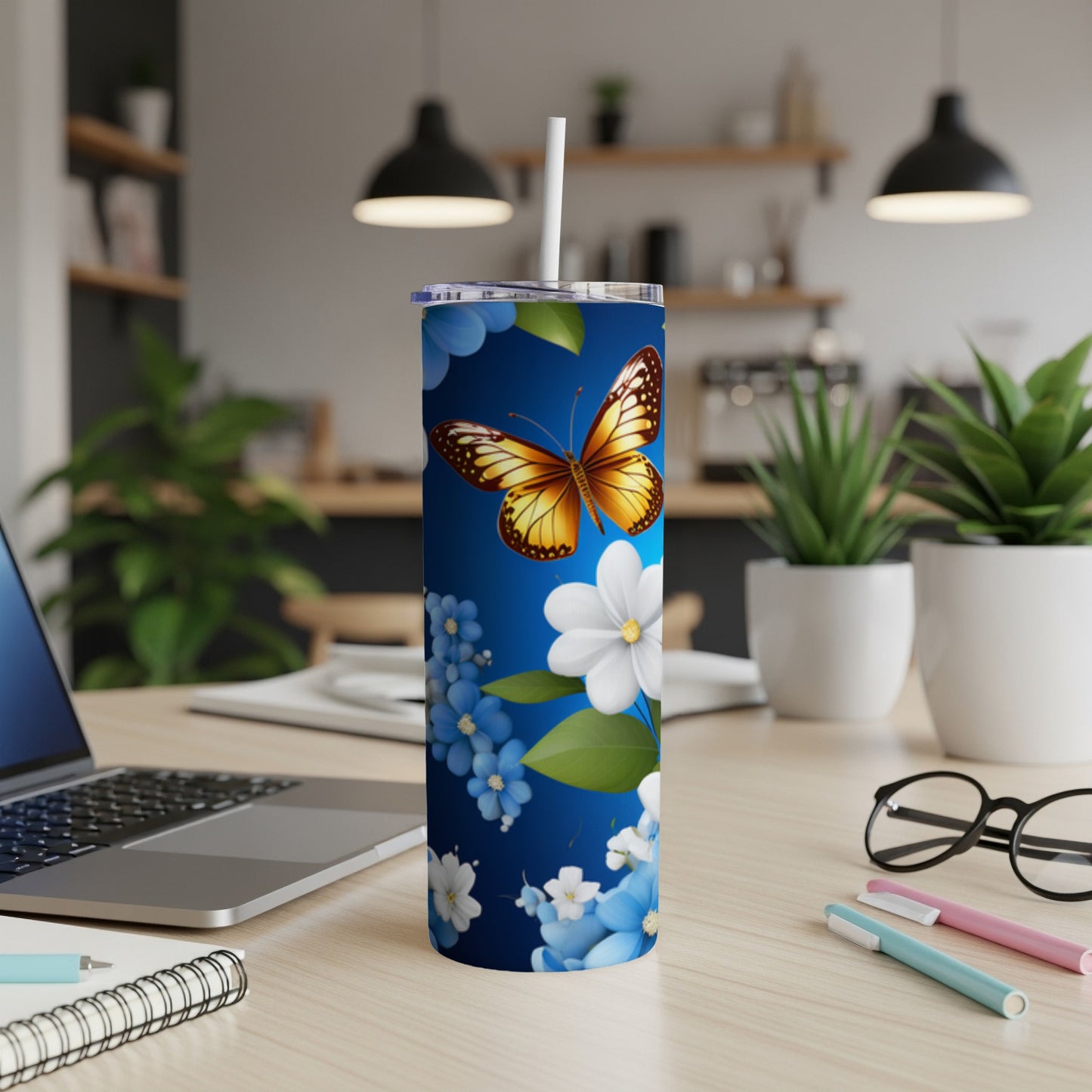Blue tumbler with a butterfly and floral design, on a desk.