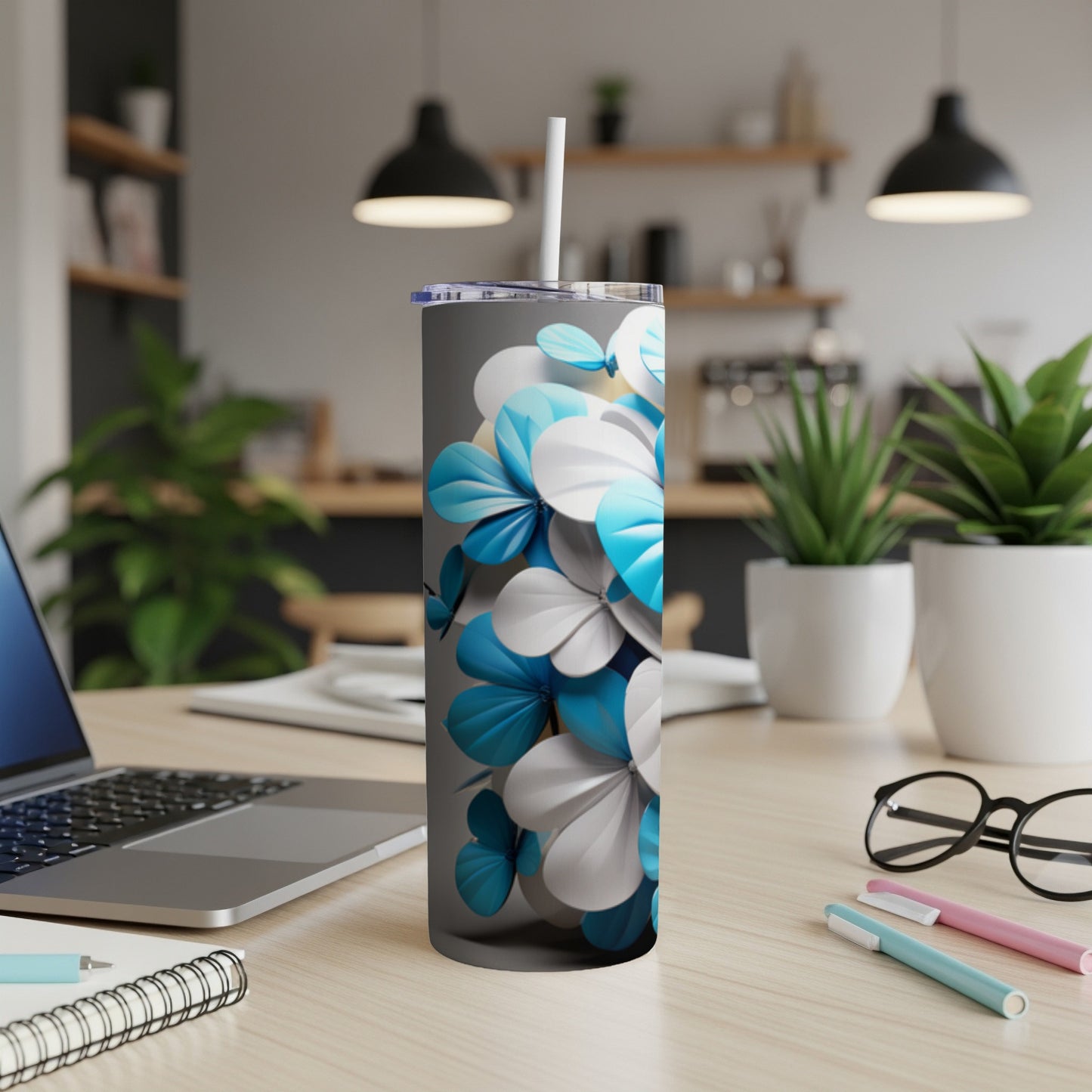 Grey tumbler with blue and white floral design, straw, on a desk.