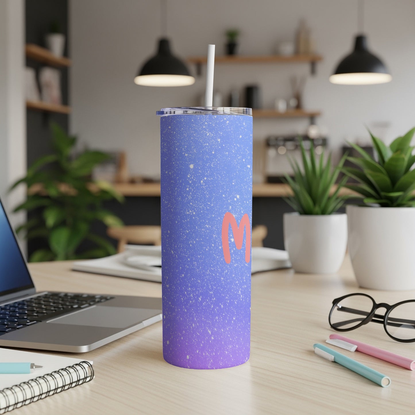 Blue and purple speckled tumbler with a pink "M" on a wooden desk.