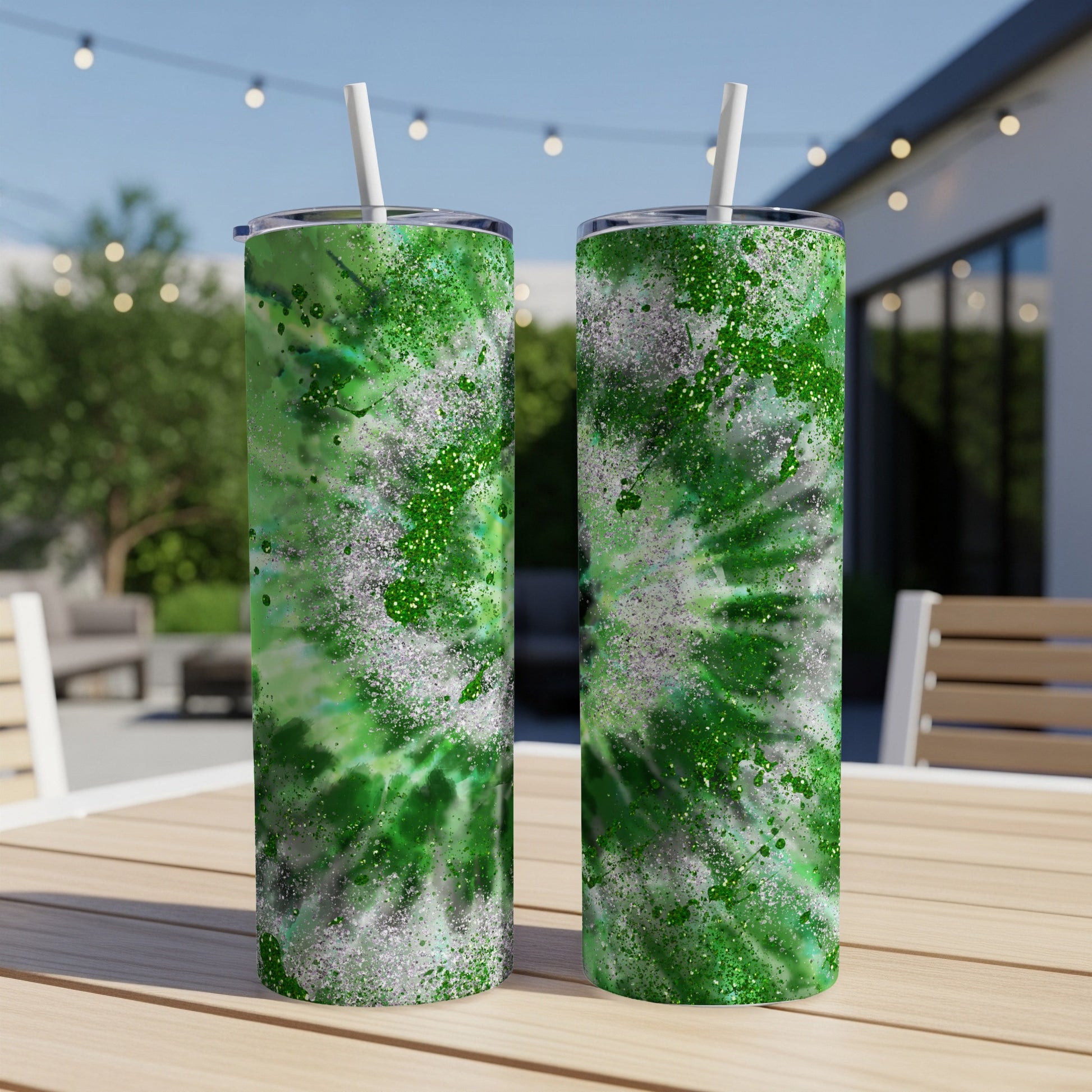 Two green tie-dye tumblers with white straws on a wooden table.