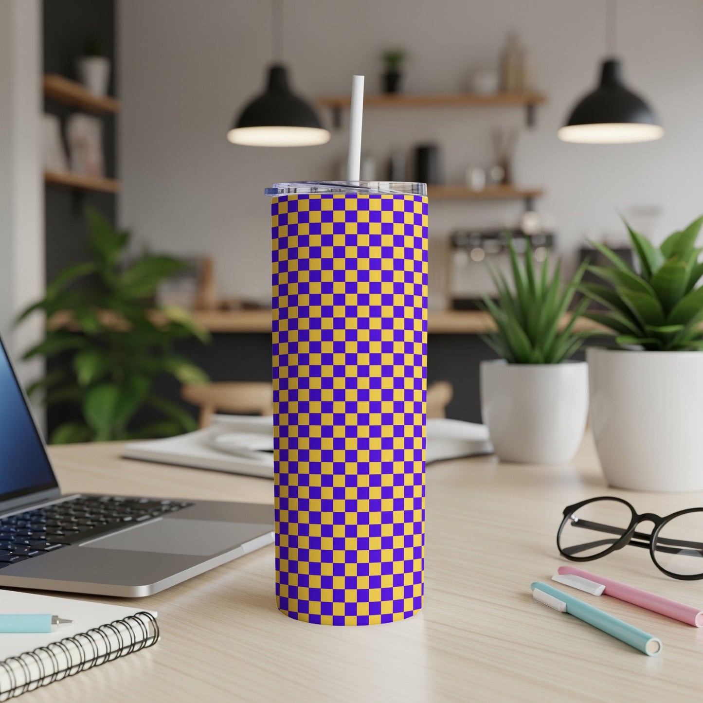 Purple and gold checkered tumbler with a white straw on a wooden desk.