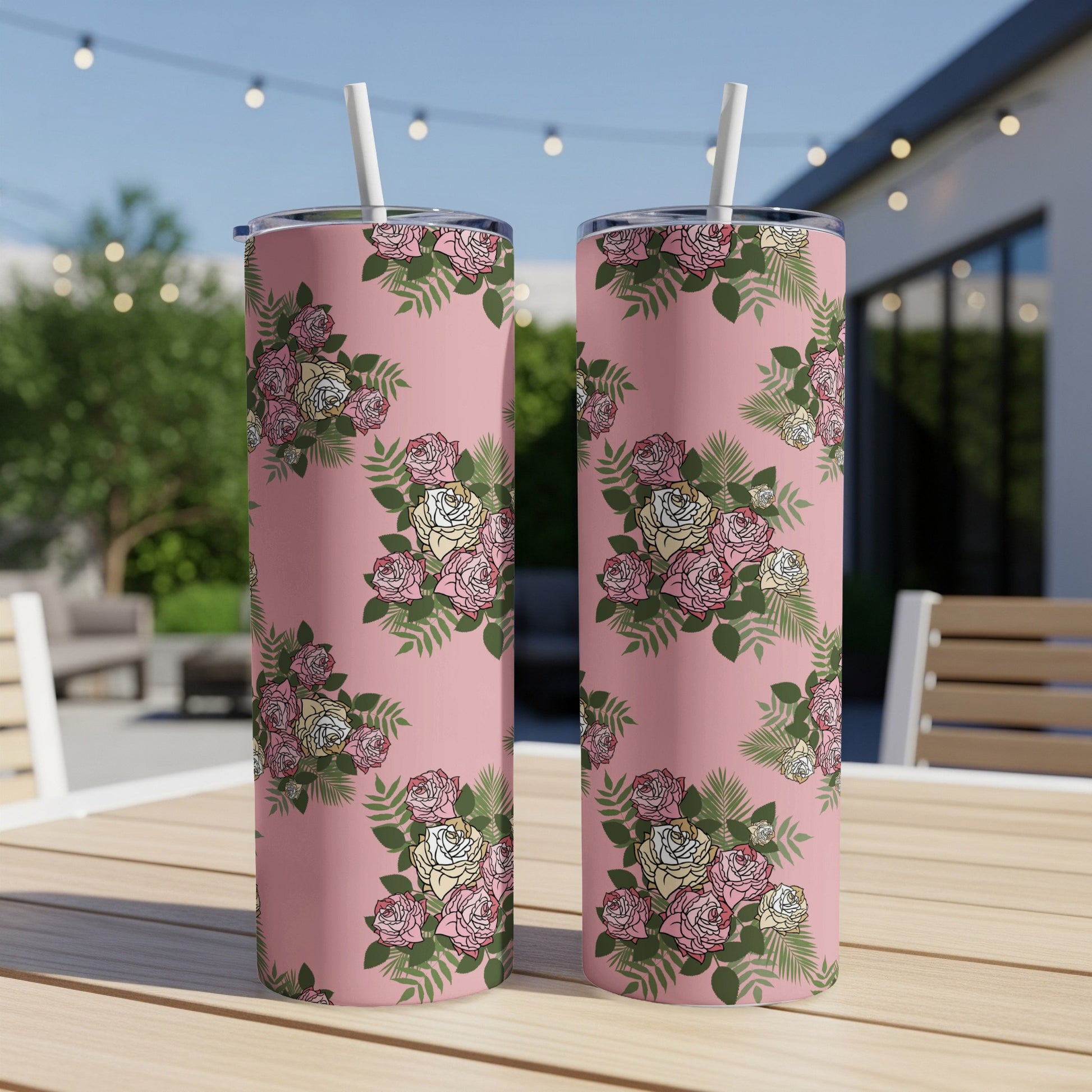Two pink tumblers with a rose floral pattern rest on a wooden table outdoors.