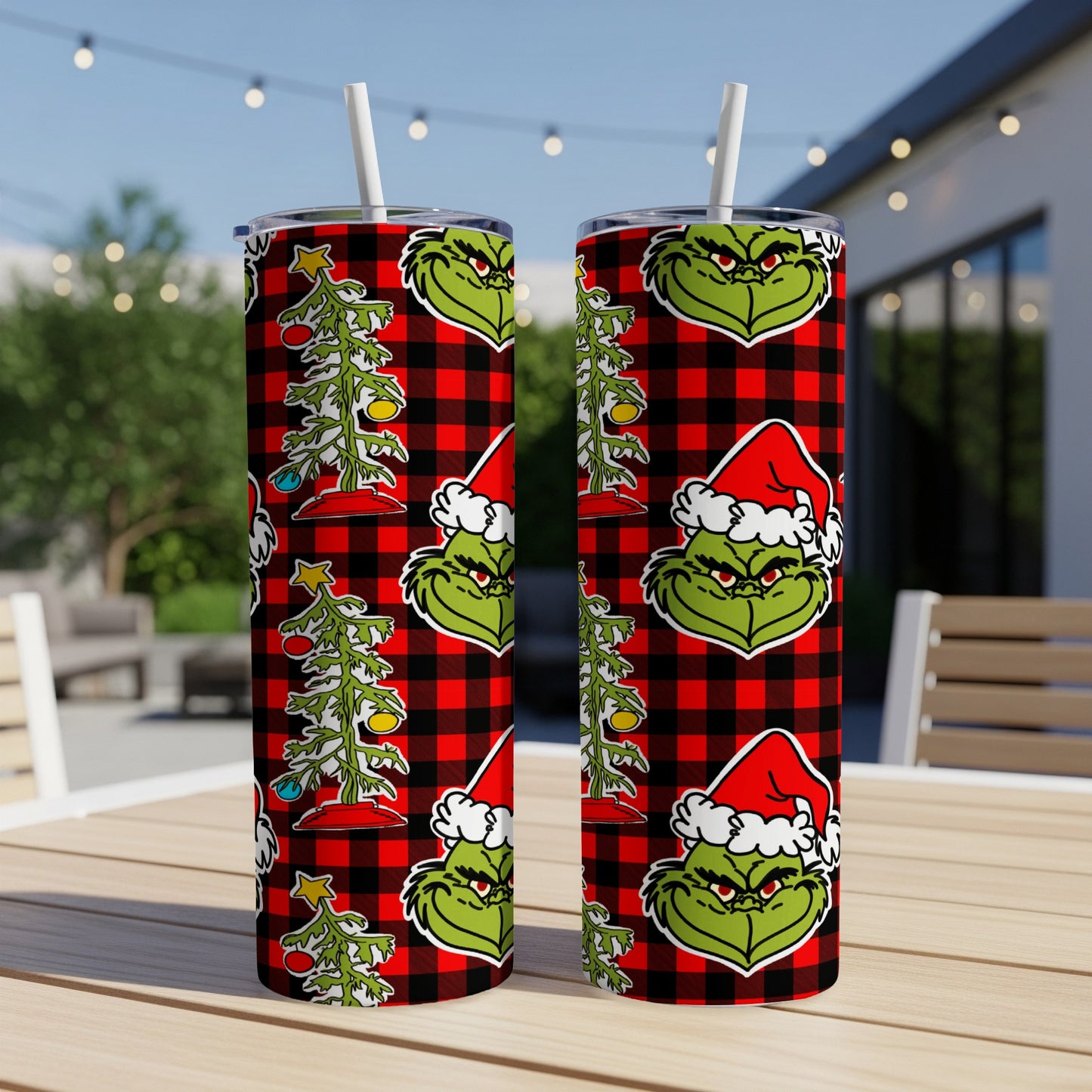 Grinch Christmas design on red plaid tumbler with straw, set on outdoor table.
