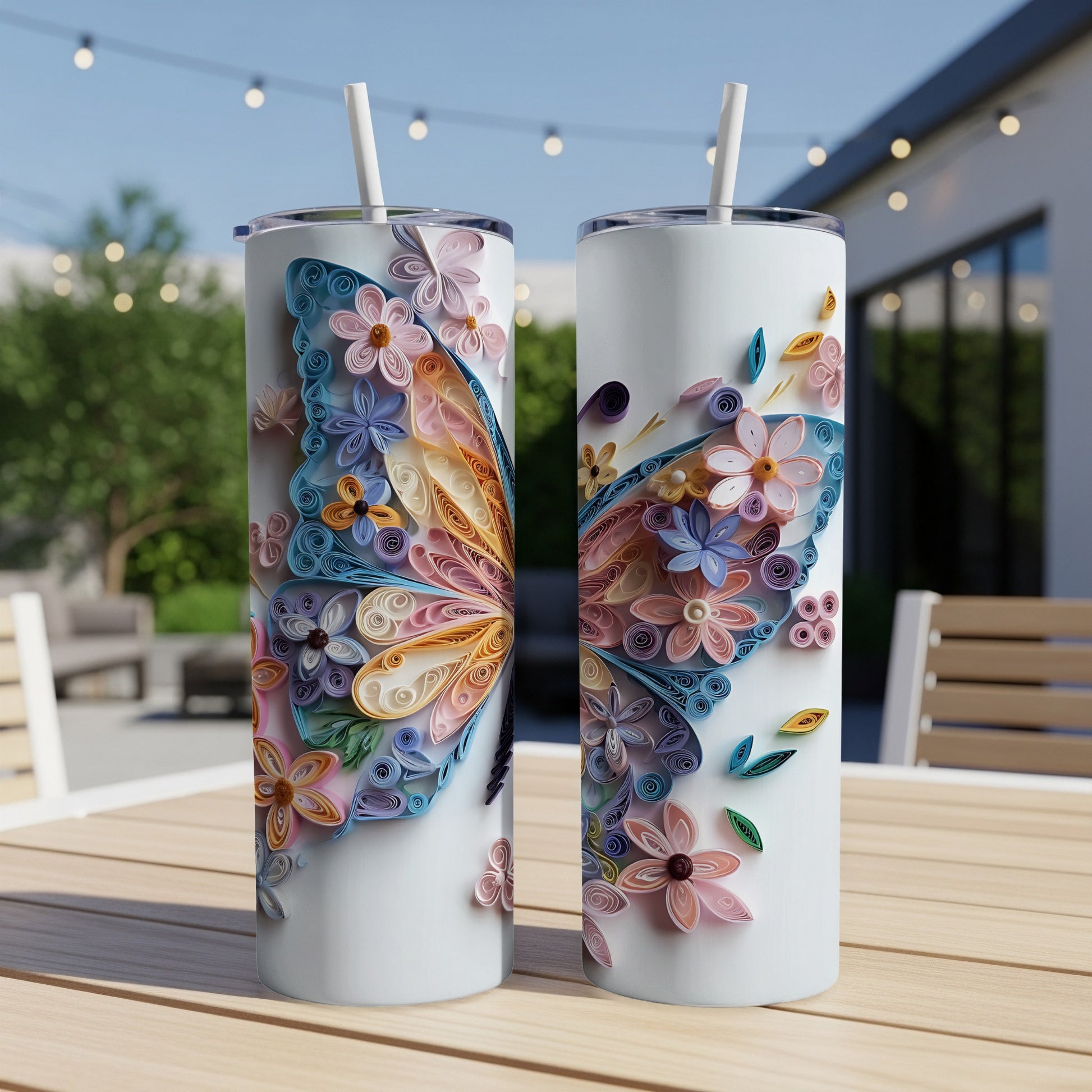 Two tumblers with colorful quilled paper butterfly designs on a wooden table outdoors.