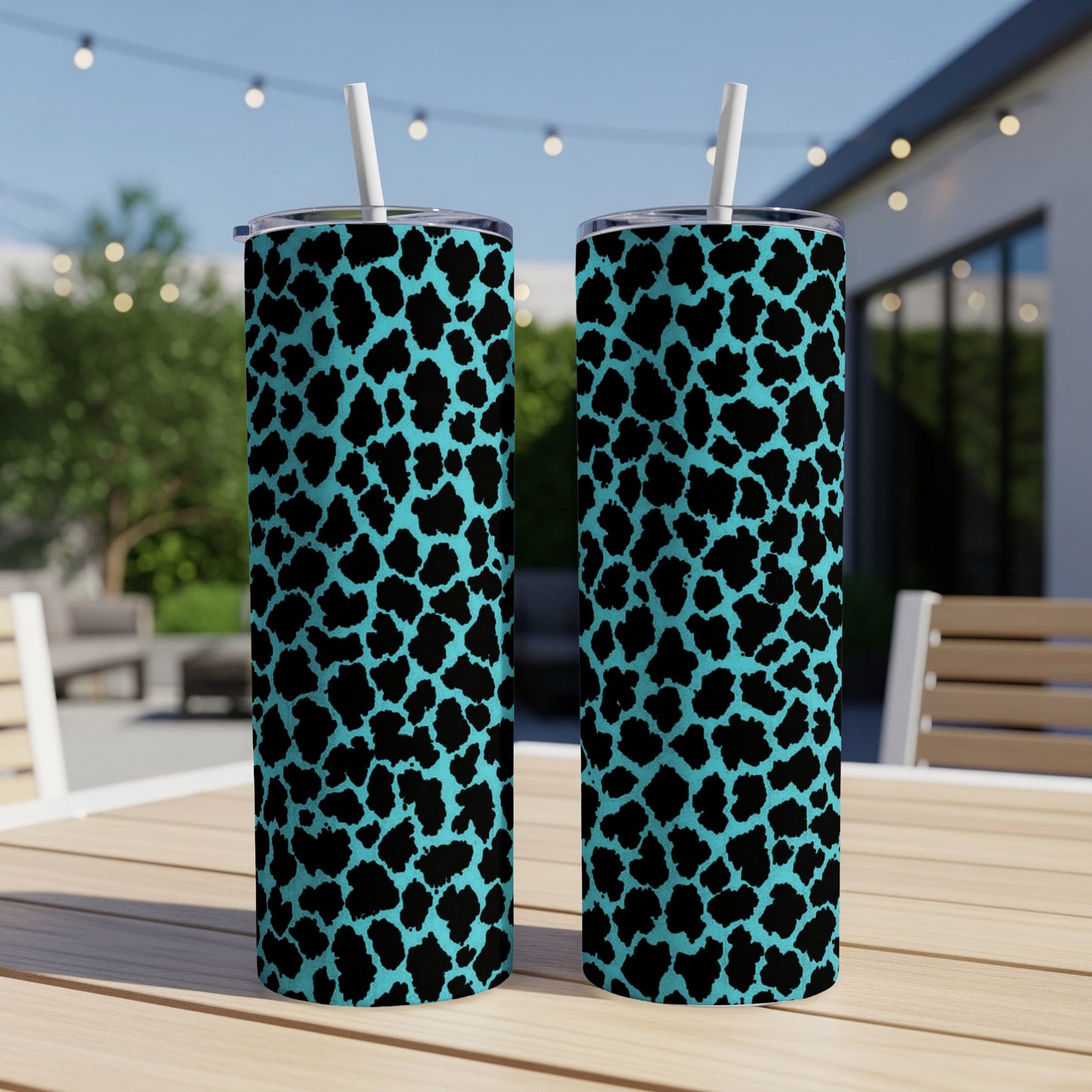 Two teal tumblers with black leopard print and white straws sit on a wooden table outdoors.