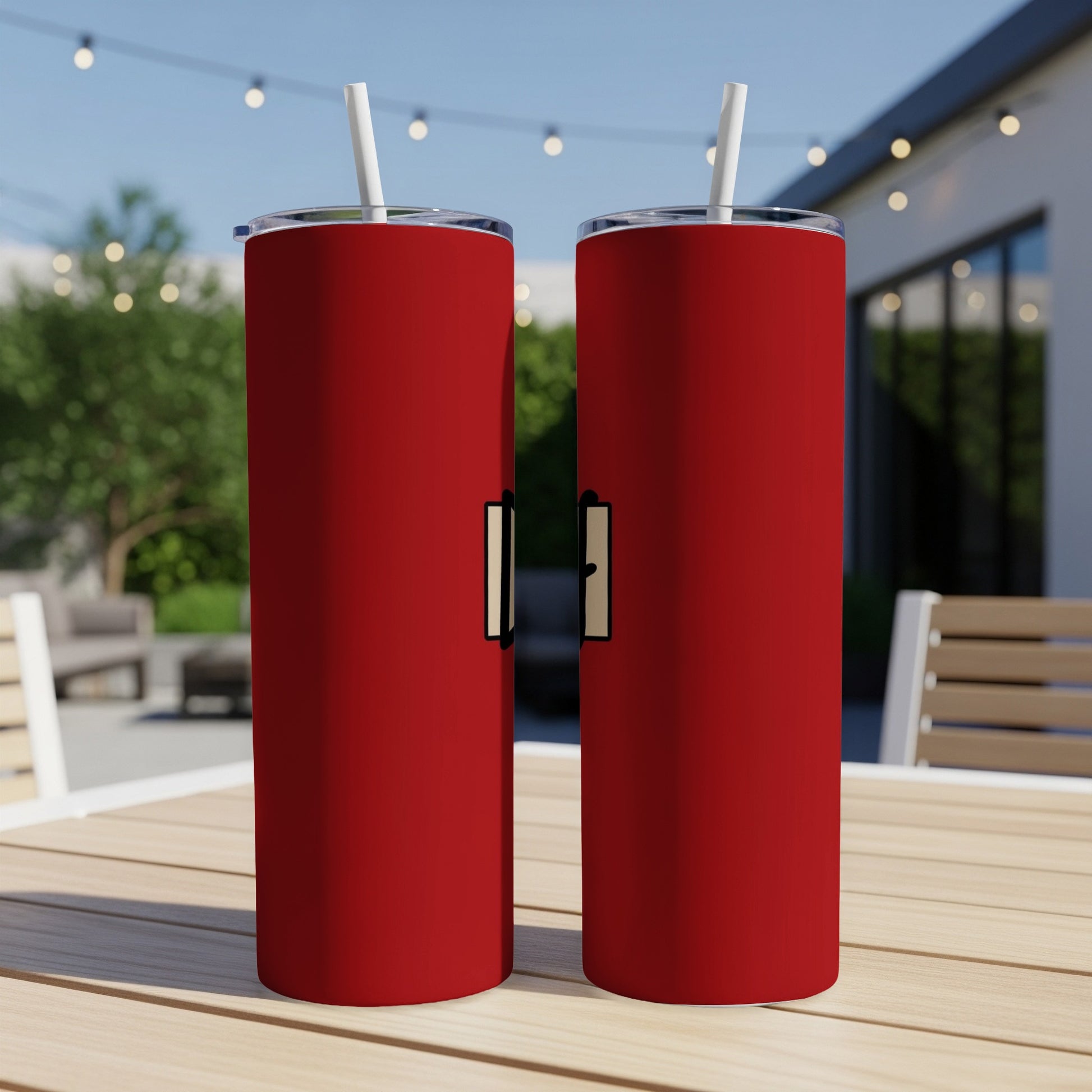Two red tumblers with white straws sit on a wooden table outdoors.