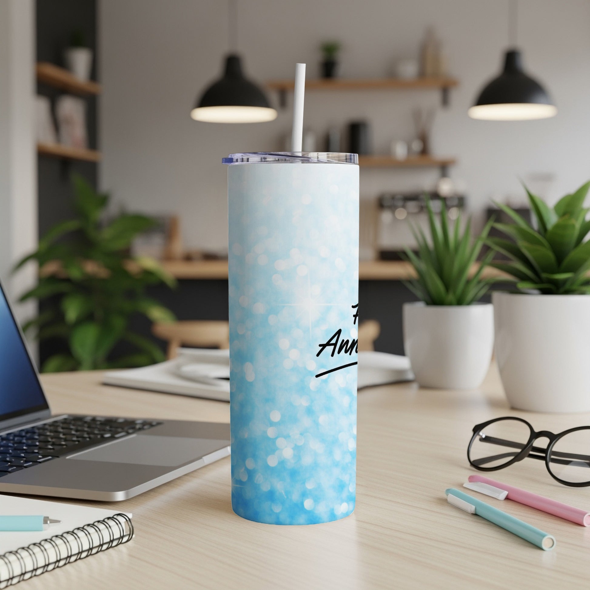 Blue glitter tumbler with "Anniversary" text and straw, on a desk.