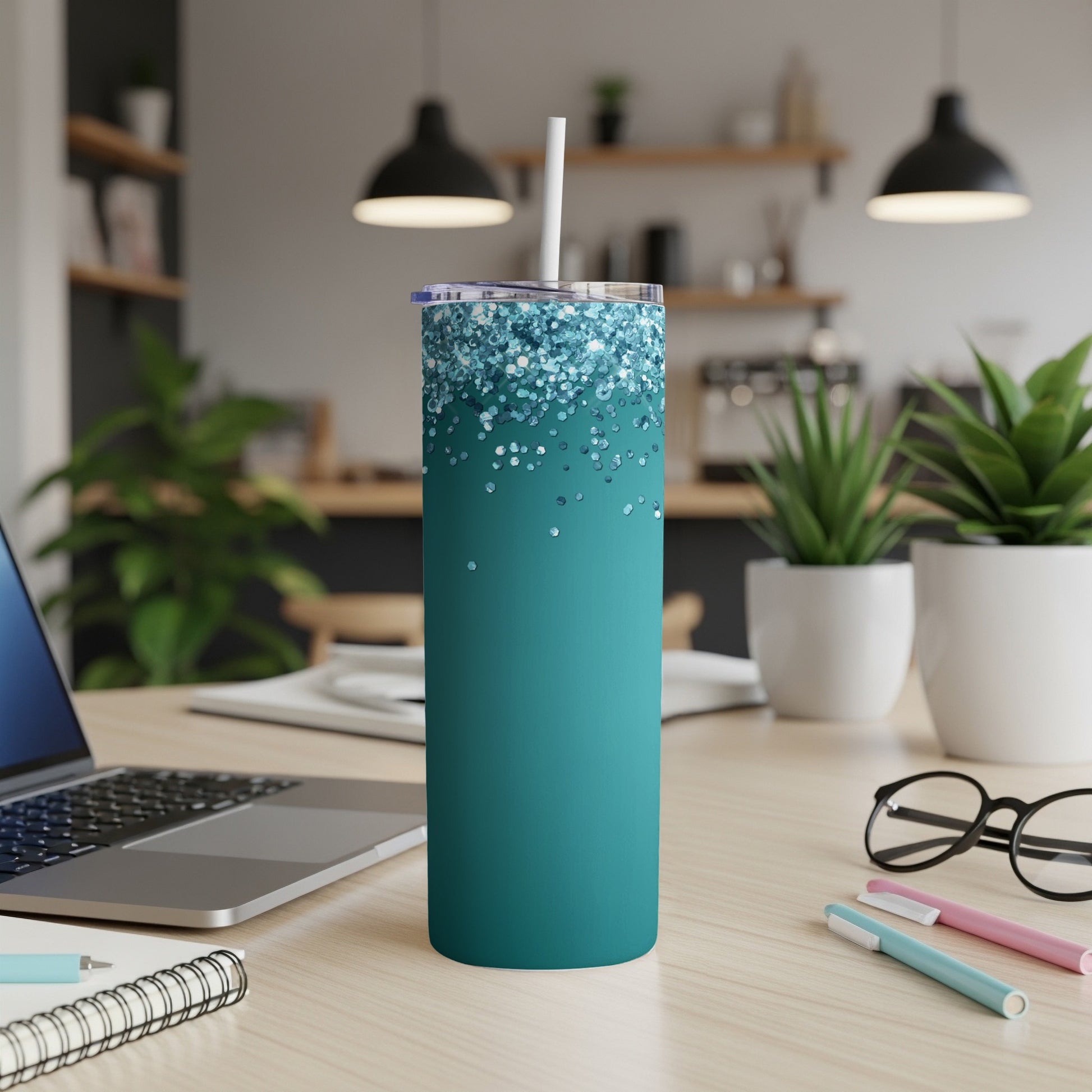 Teal tumbler with glittering top and white straw on a desk.